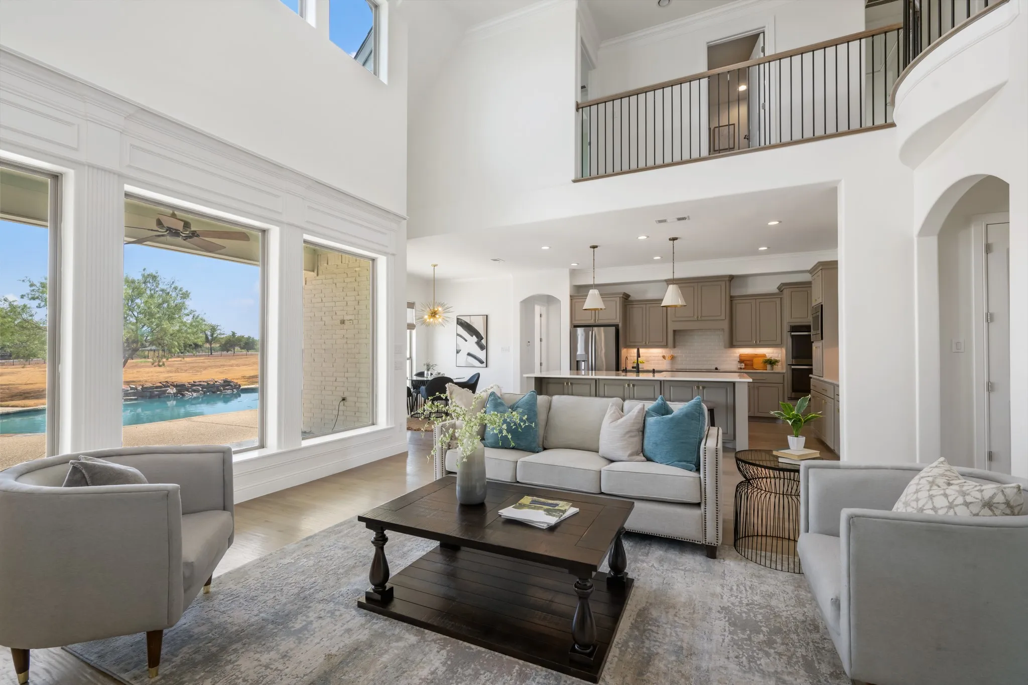 Vaulted ceilings, expansive windows, open-concept design, large kitchen island with pendant lighting, and a second-story interior balcony with metal railing