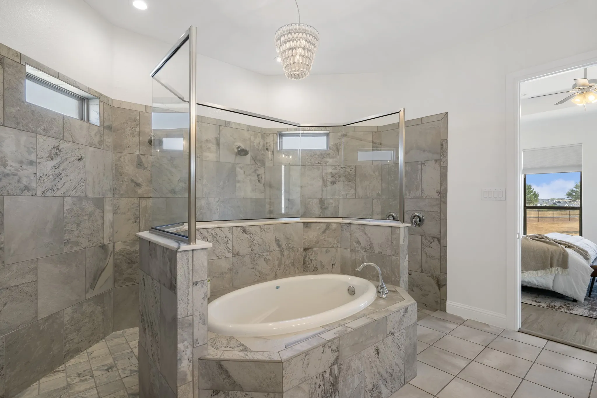 Spacious bathroom featuring a built-in soaking tub, a walk-in shower with glass enclosure, tiled walls and flooring, and a chandelier-style light fixture
