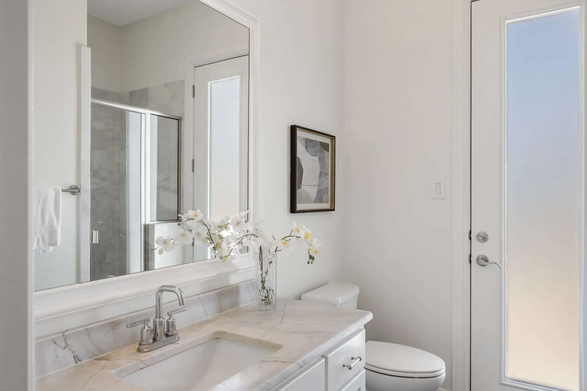 White vanity with a stone countertop, an undermount sink, and a framed mirror