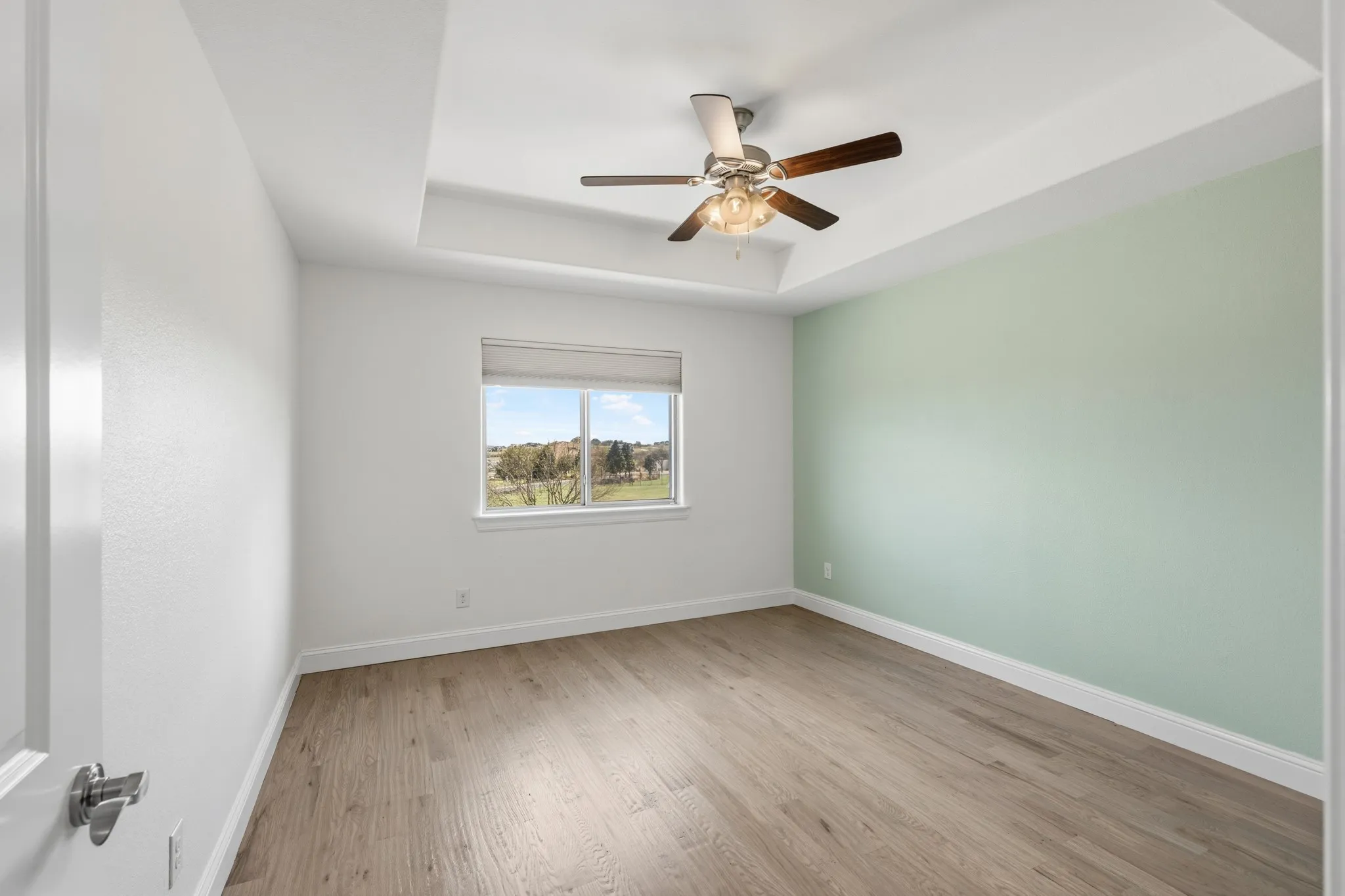 Room featuring wood-finish flooring, a tray ceiling, and a ceiling fan with light fixture