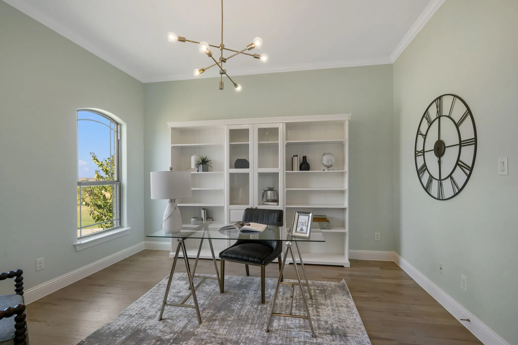 Arch-top window, wood-finish flooring, built-in shelving, crown molding, and a modern chandelier