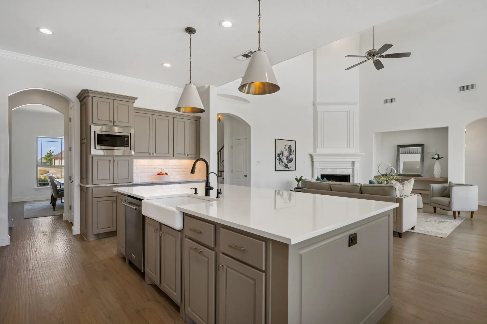 Kitchen island with white countertop and farmhouse sink, wood-finish flooring, vaulted ceiling with ceiling fan, fireplace with detailed mantel, and recessed lighting