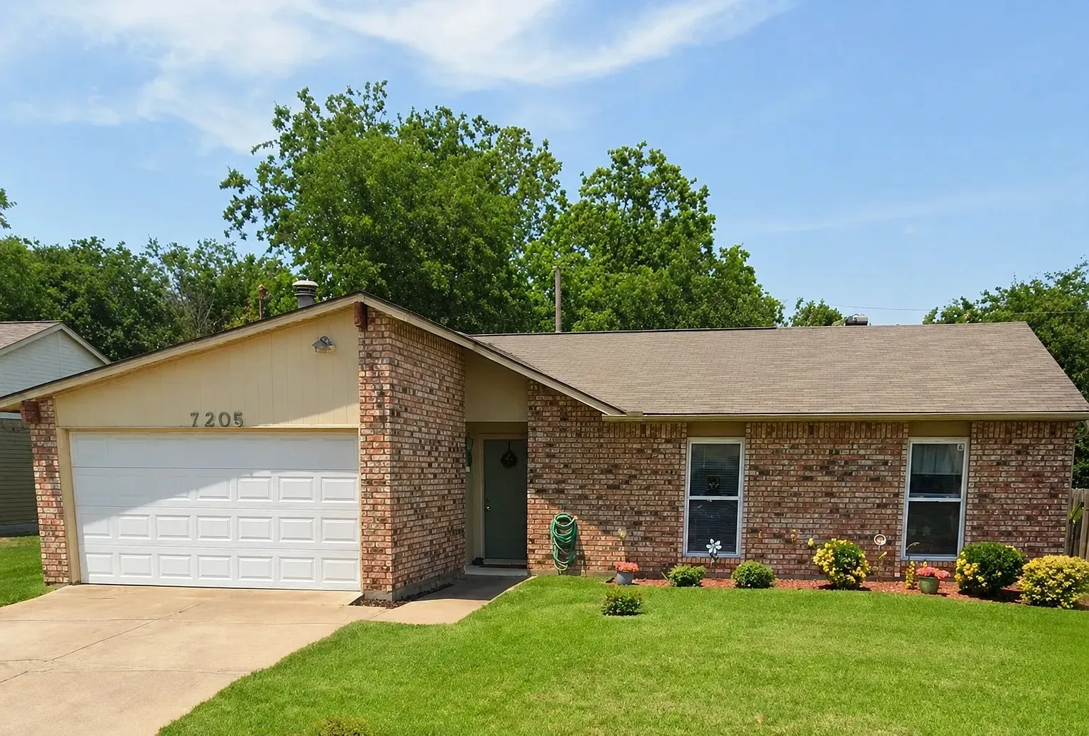 Brick exterior with a peaked roofline, attached garage, and a concrete driveway