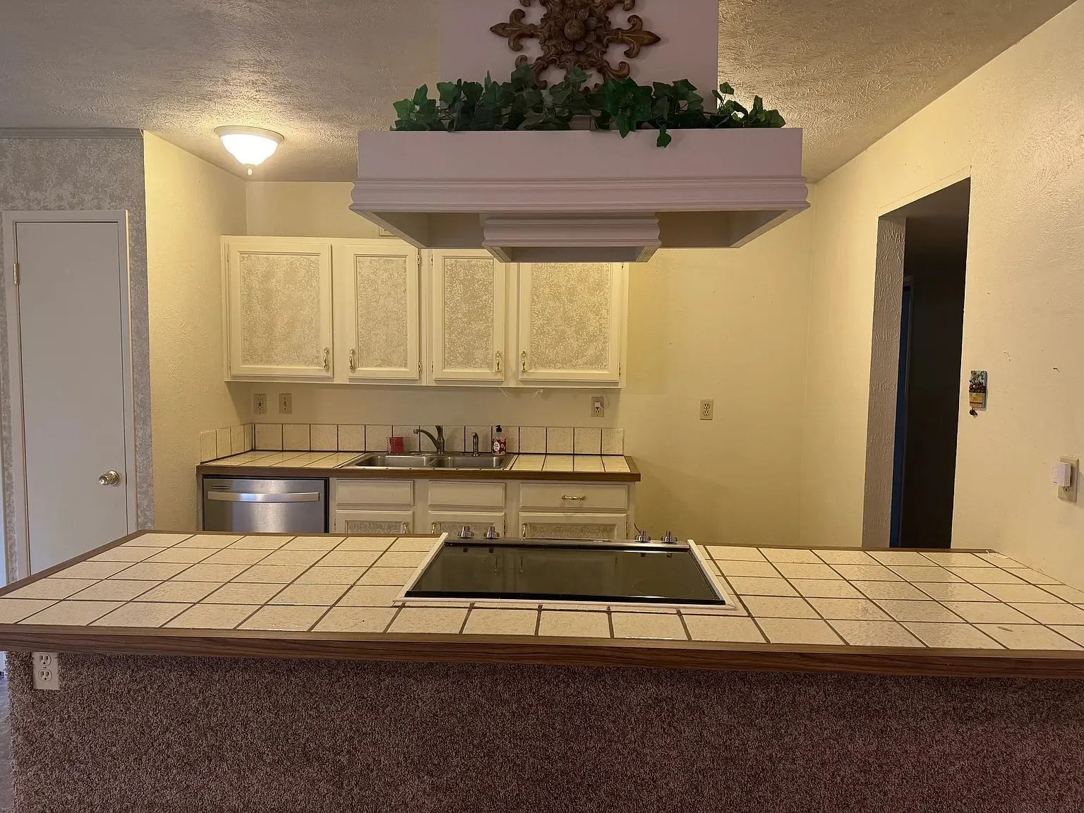 Kitchen featuring white cabinetry, tile countertops, a built-in cooktop, and a stainless steel dishwasher