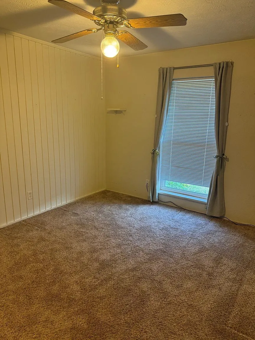 Carpeted room with a window, vertical paneling detail on one wall, and a ceiling fan with light fixture
