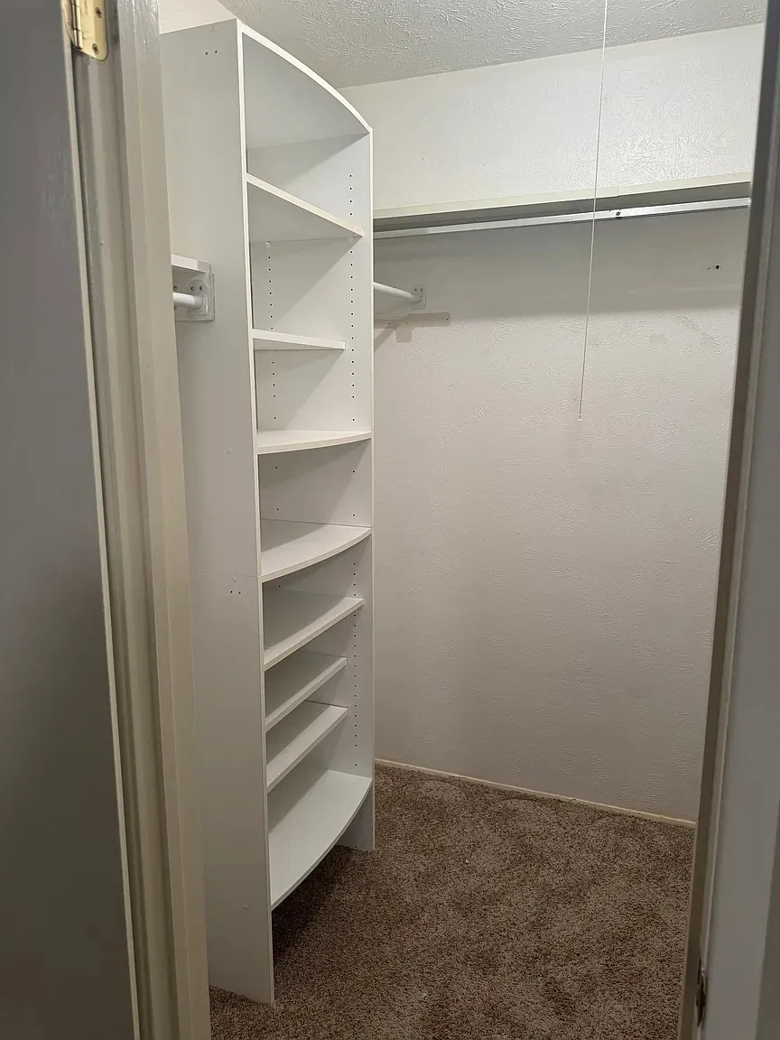 Built-in shelving system with adjustable white shelves, clothing rod, and neutral carpet flooring