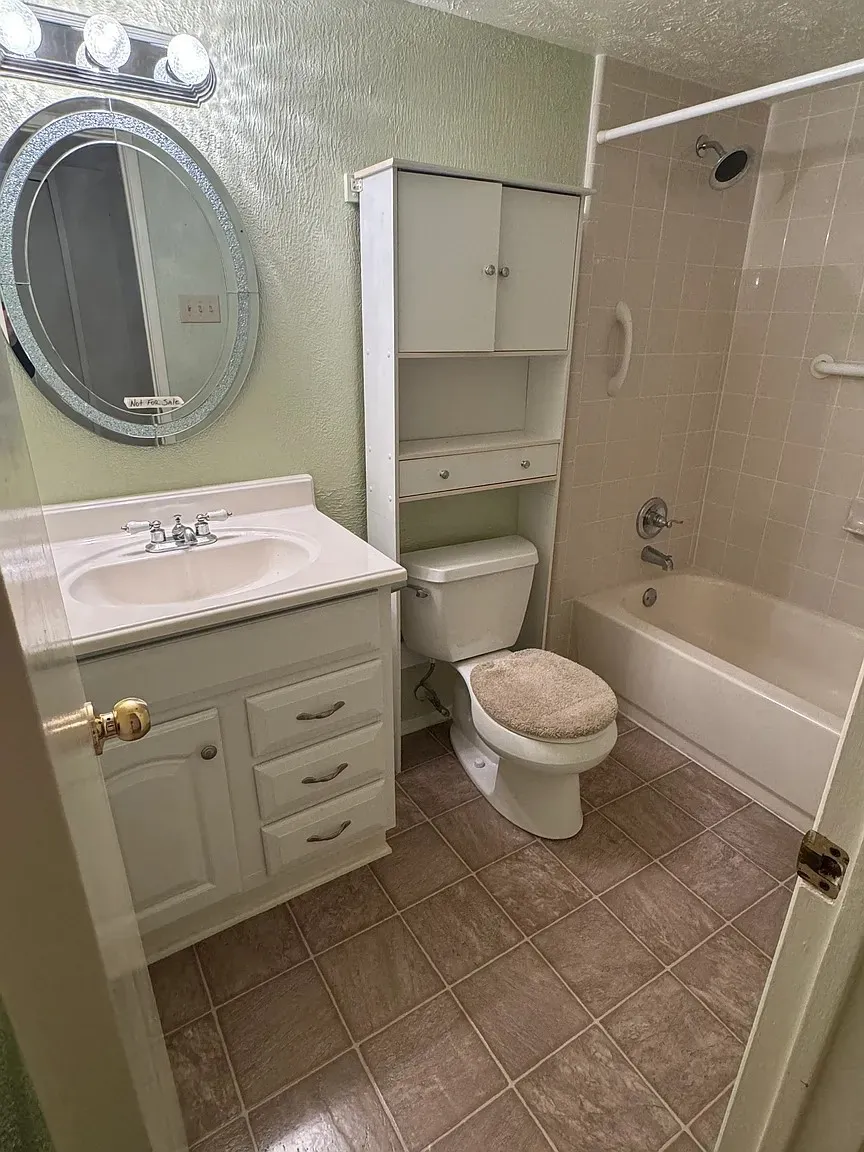 Vanity with integrated sink, coordinating cabinet storage, tiled flooring, and a shower-tub combination with grab bars