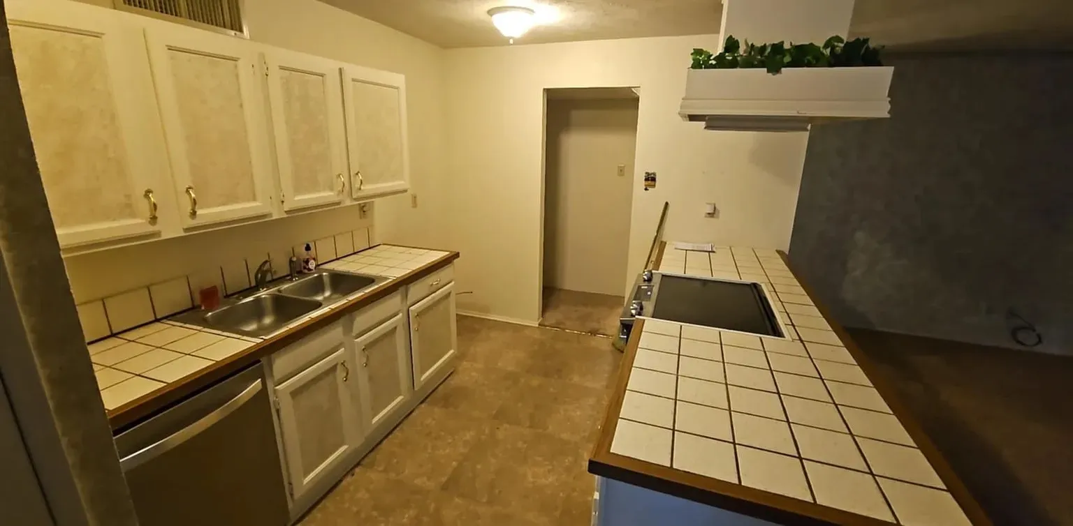 Kitchen featuring dual basin stainless steel sink, tile countertops, white cabinetry with gold-tone hardware, and a built-in cooktop