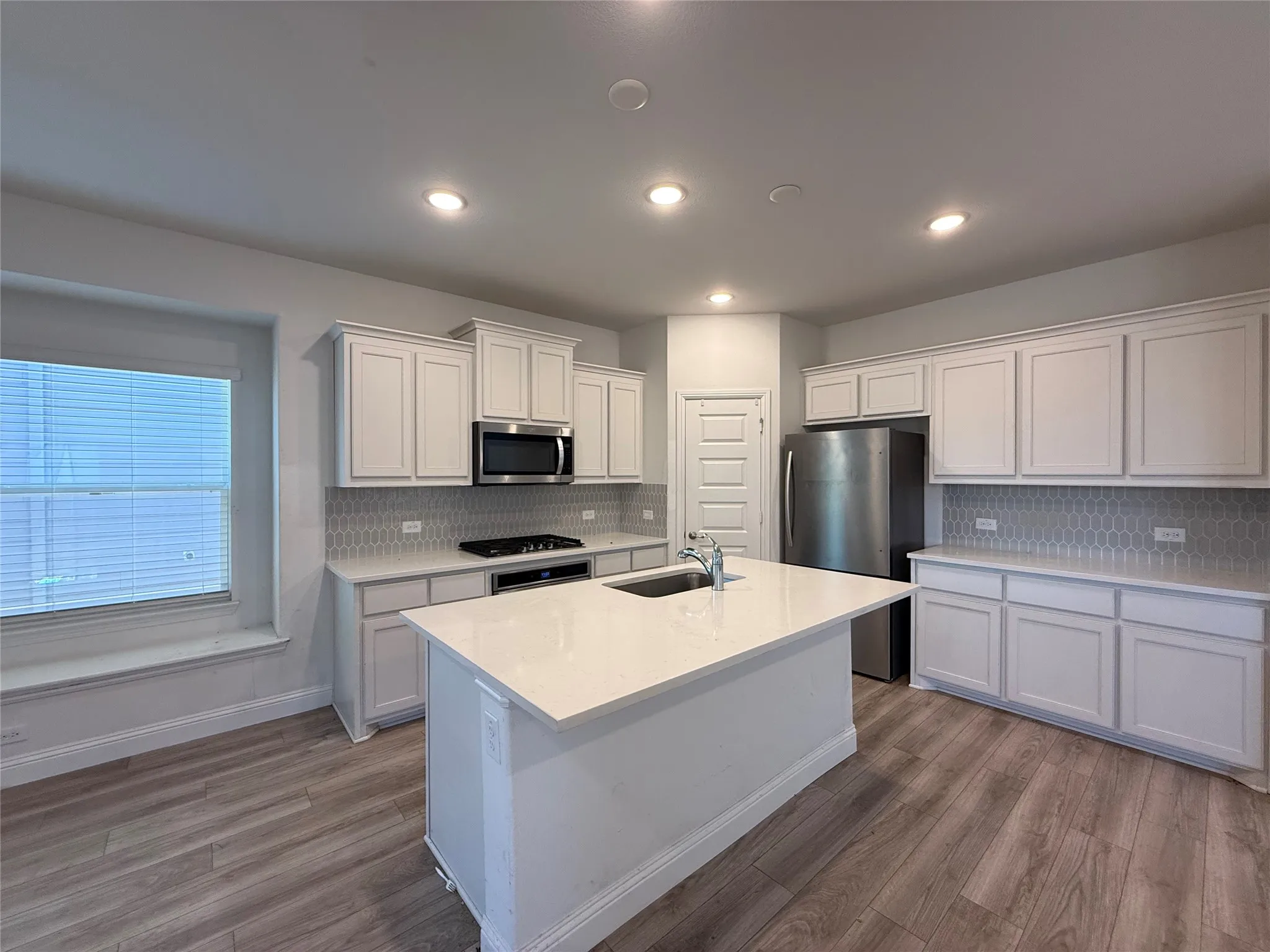 Kitchen featuring white cabinetry, light-toned countertops, a stainless steel microwave, a built-in cooktop, and wood-finish flooring
