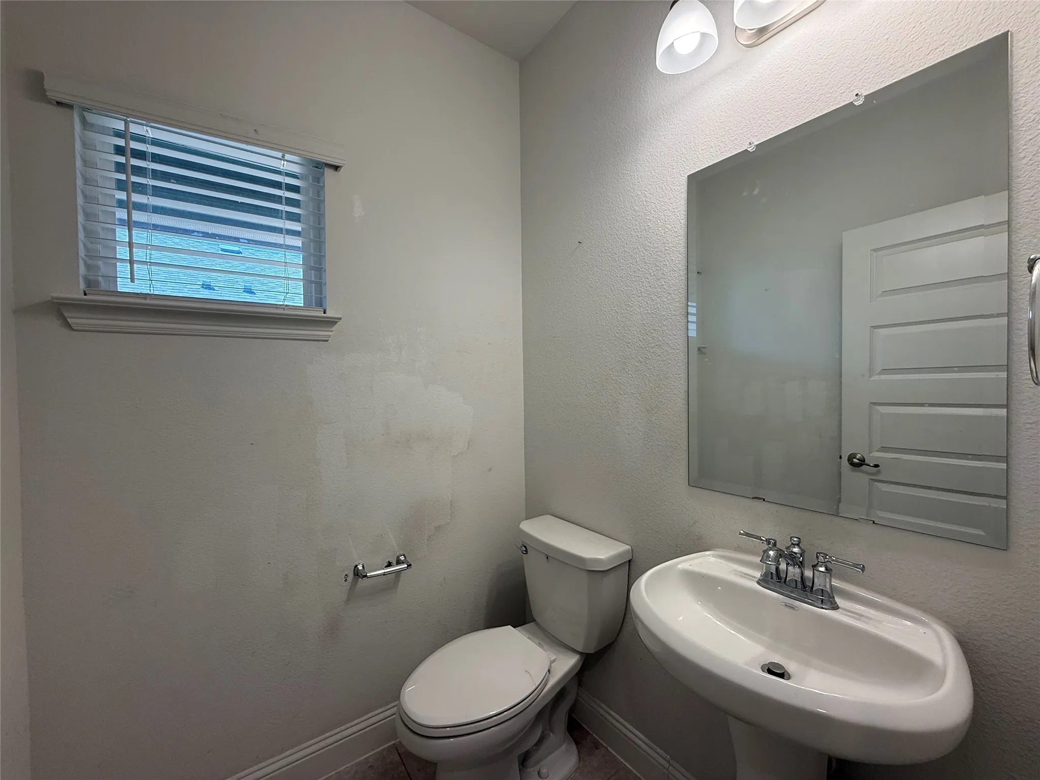 Pedestal sink with chrome faucet, wall-mounted mirror, and overhead vanity lighting