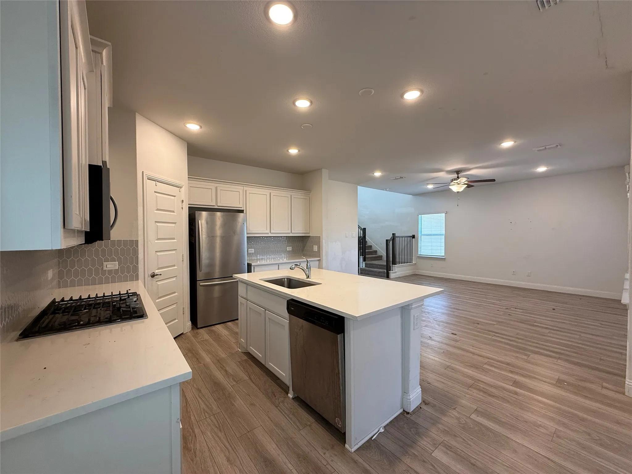 Open-concept kitchen featuring an island with an integrated sink and dishwasher, white cabinetry, stainless steel appliances, and wood-finish flooring