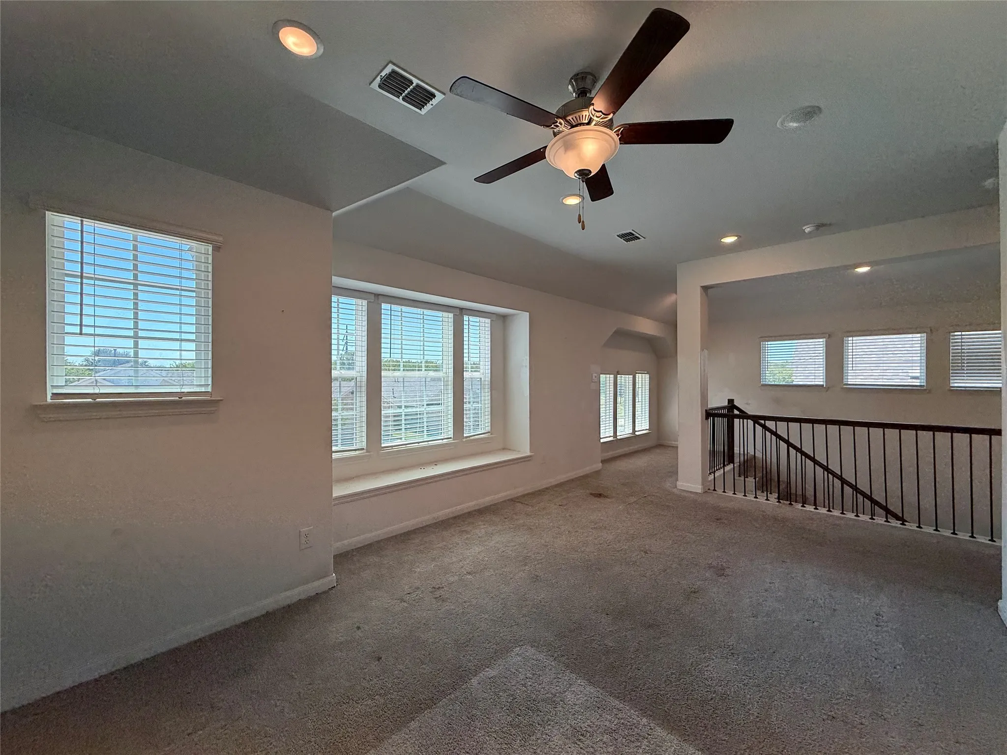 Spacious carpeted area with a ceiling fan, recessed lighting, multiple windows, and a built-in window bench