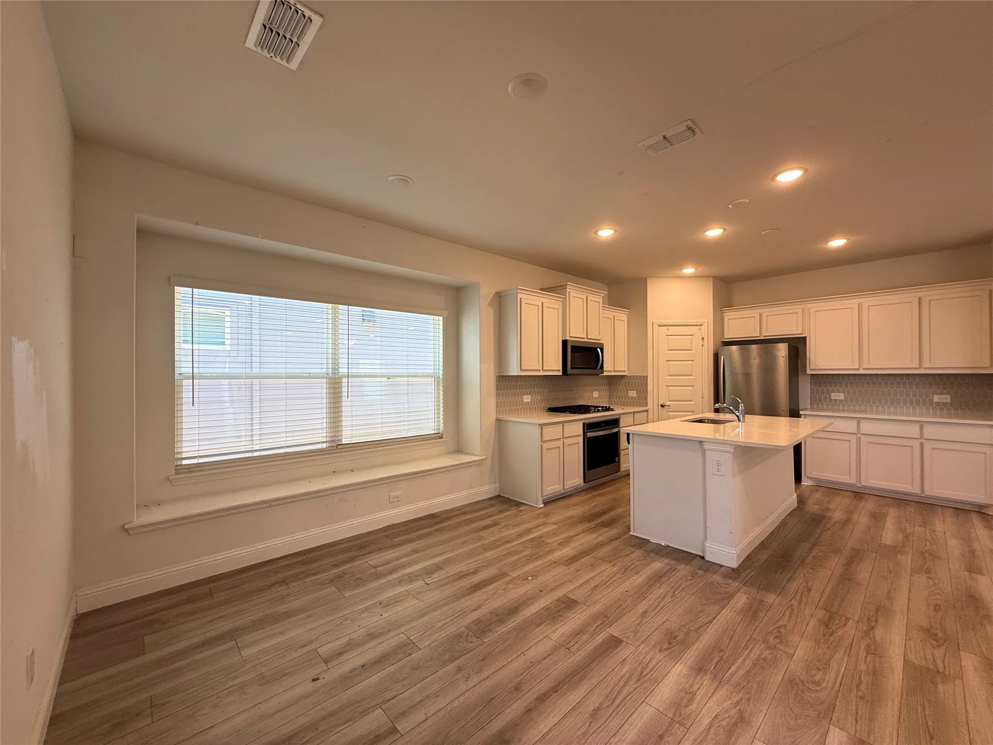 Kitchen featuring a center island with sink, stainless steel appliances, white cabinetry, and light-colored countertops