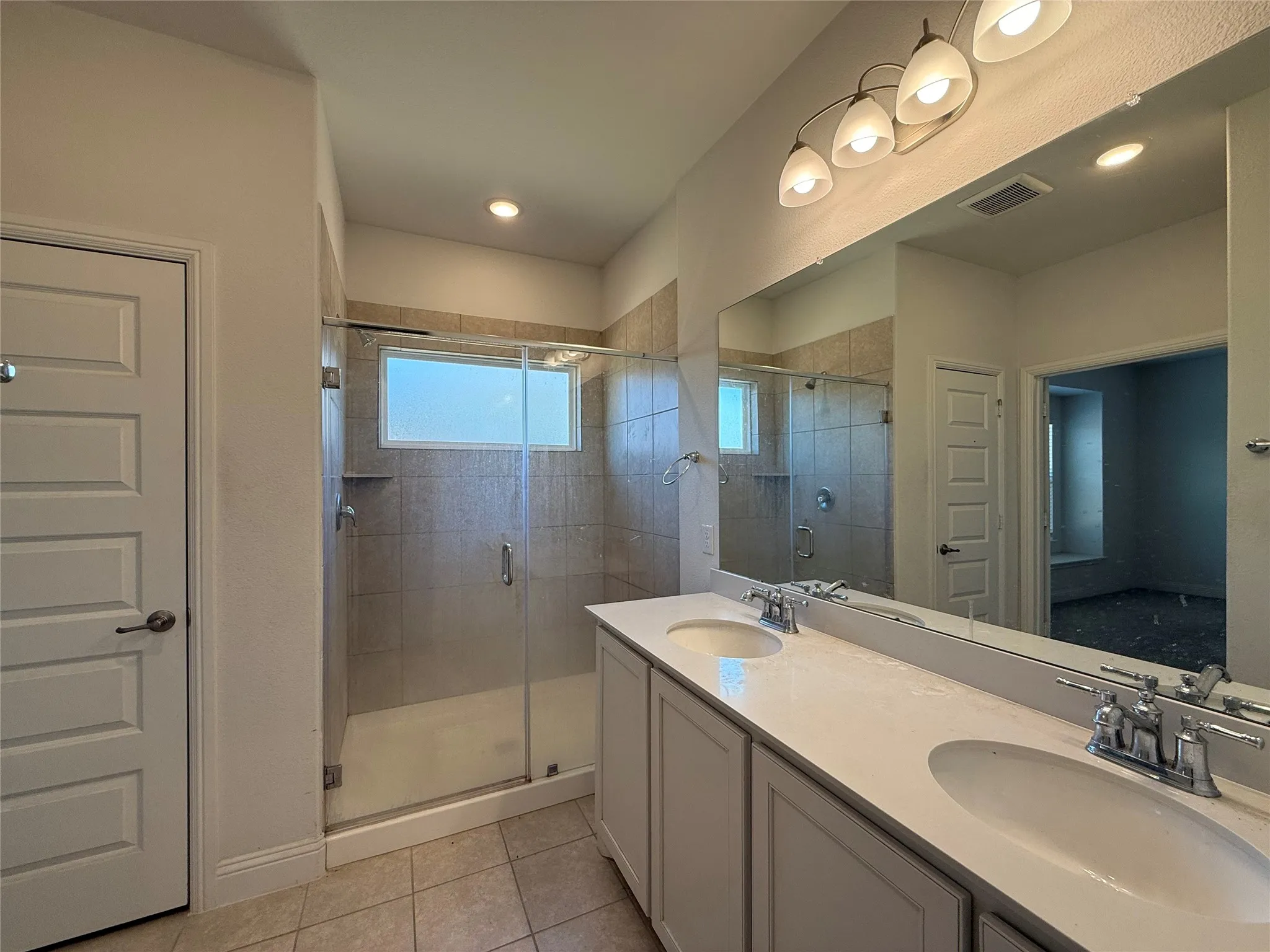 Dual sink vanity with white countertops, expansive wall-mounted mirror, and tile flooring