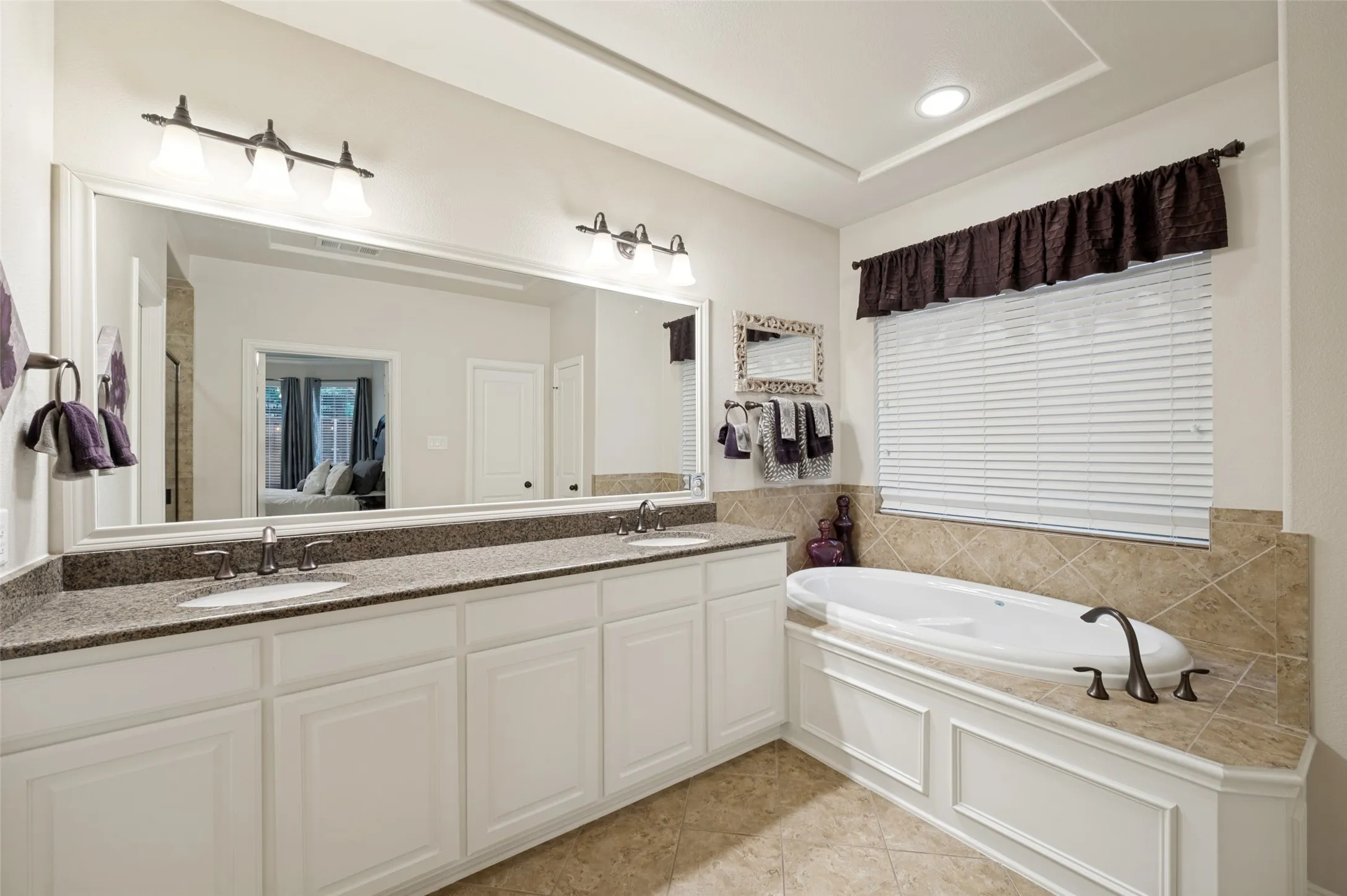 Spa-inspired primary bathroom featuring dual vanities with an oversized framed mirror, a relaxing soaking tub beneath a large window, and a spacious layout designed for everyday comfort and luxury.