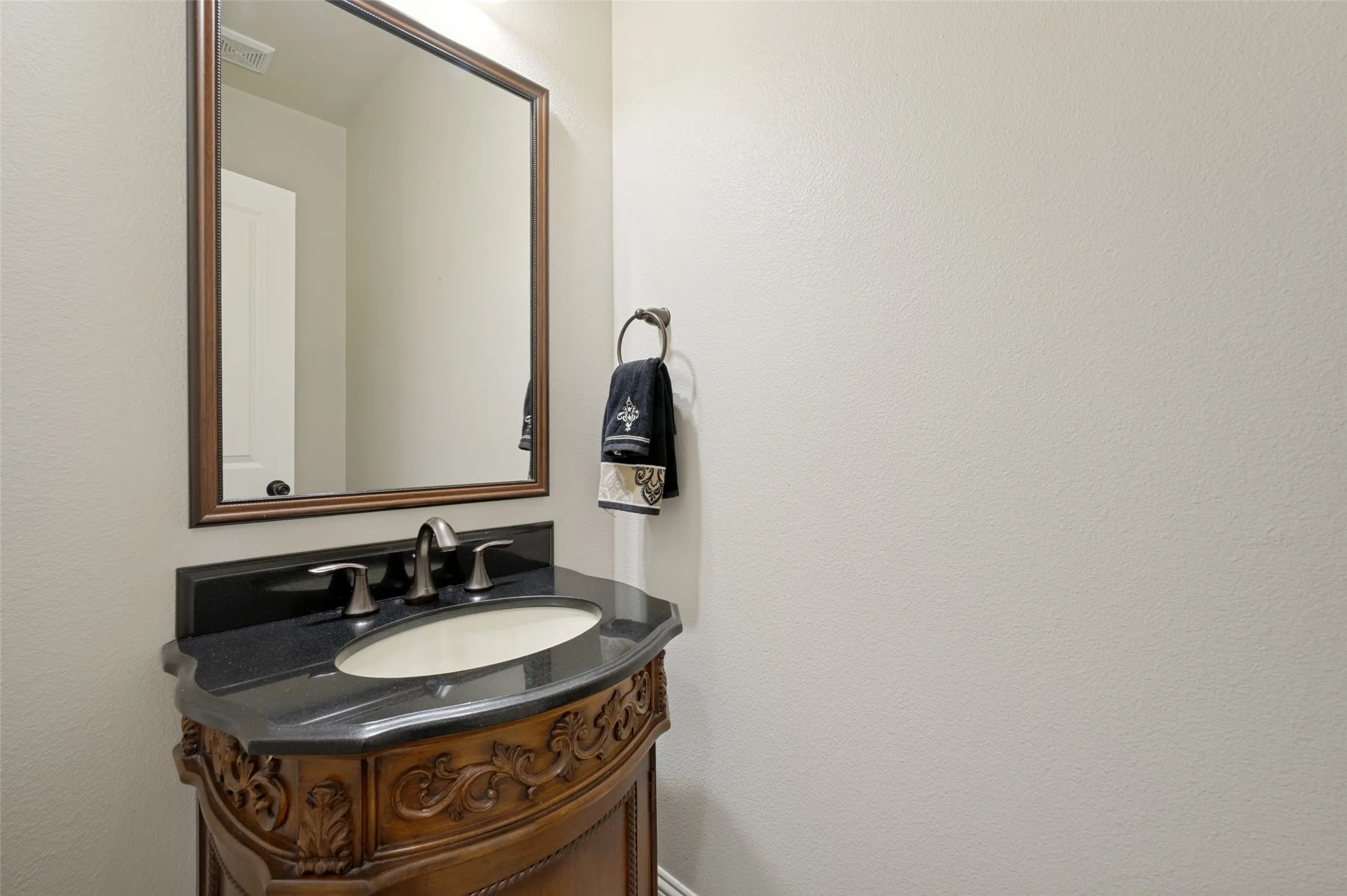 Conveniently located powder bath featuring an upgraded furniture-style vanity with granite countertops, an undermount sink, and a framed mirror that adds a touch of elegance for guests.