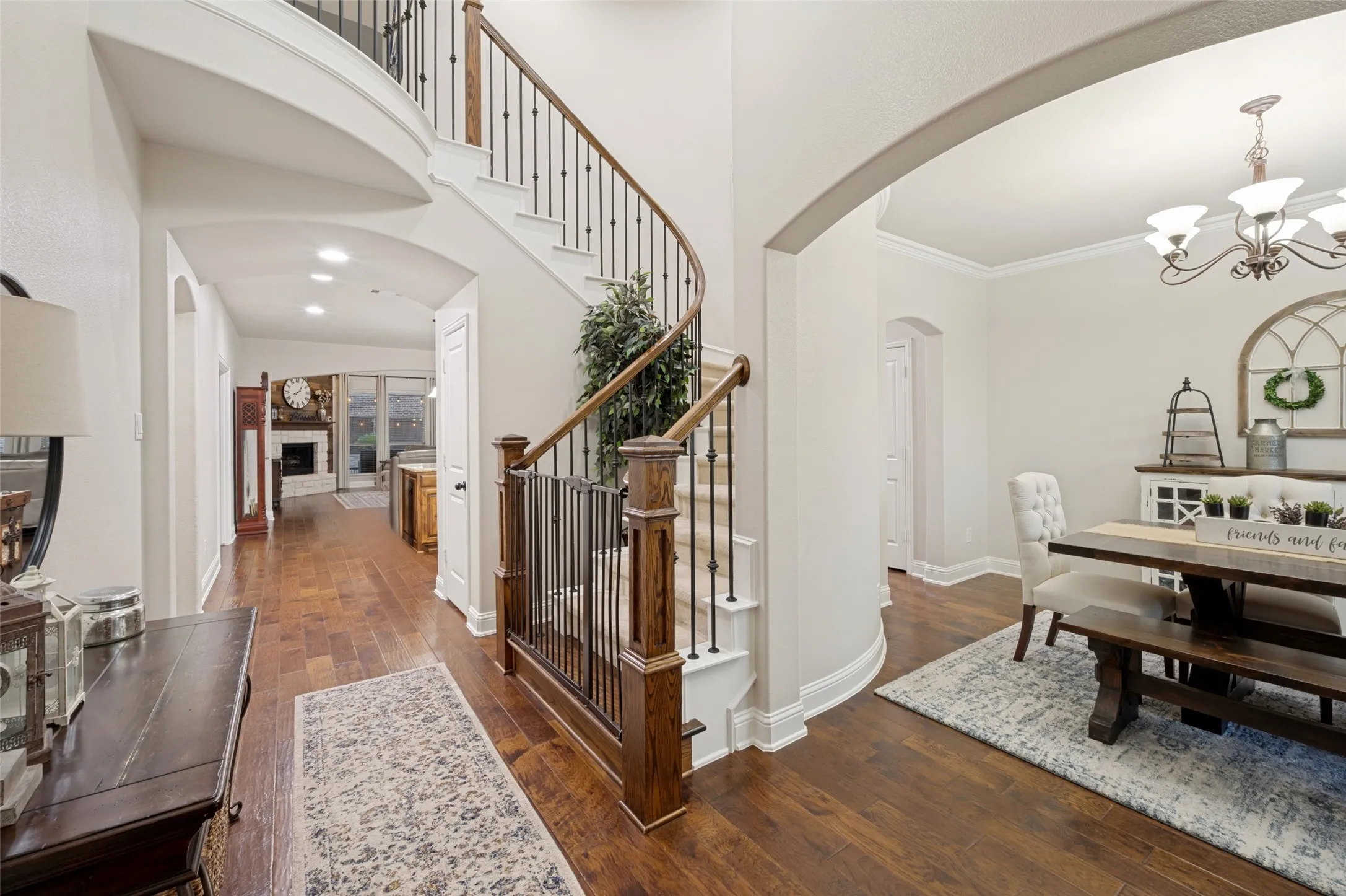 Step inside to an inviting foyer featuring warm wood floors, an elegant curved staircase with wrought iron accents, and an open design that flows effortlessly into the main living areas.