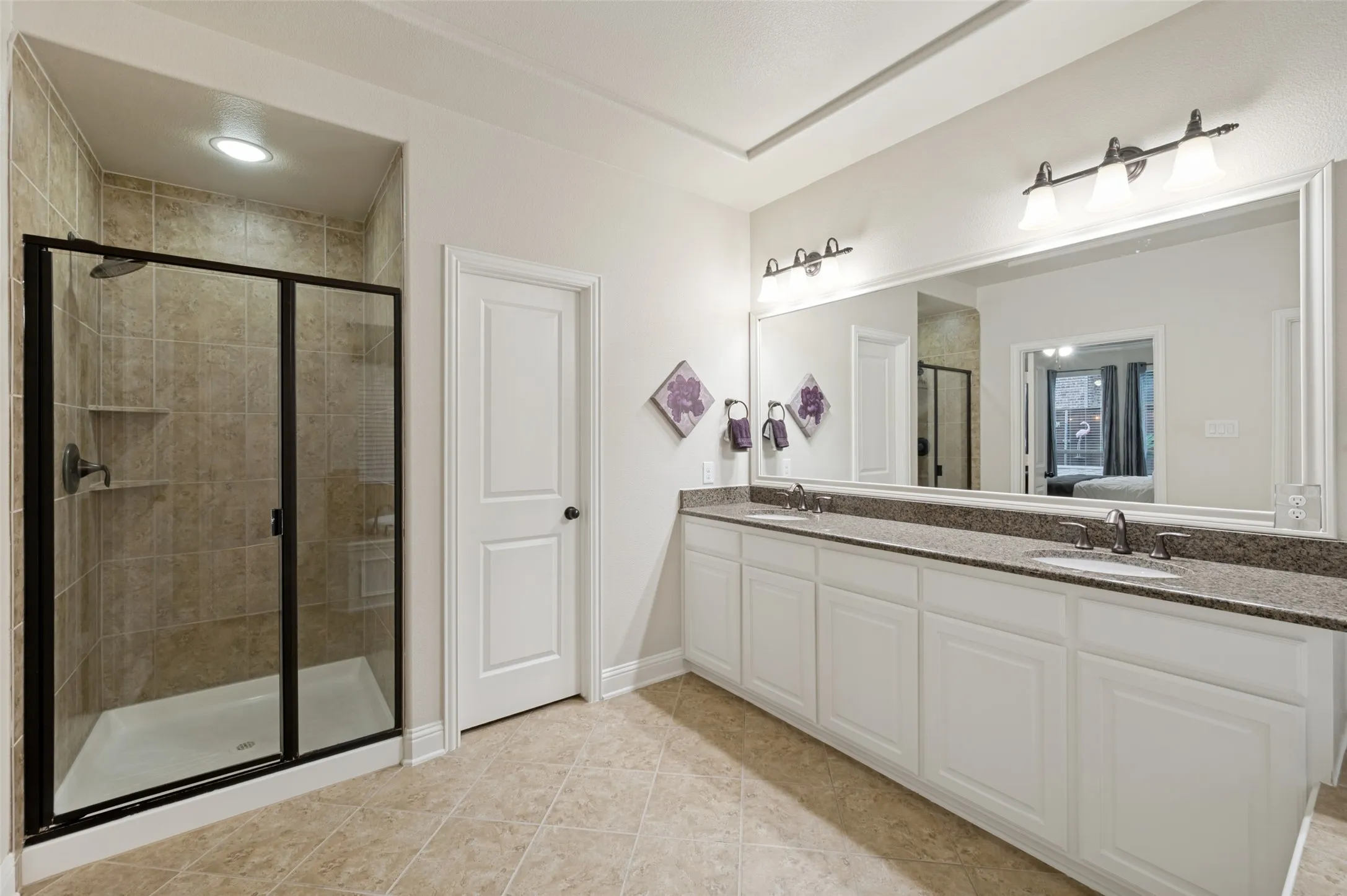 Luxurious primary bathroom featuring an oversized dual-sink vanity with an expansive mirror, a spacious walk-in shower with framed glass enclosure, and elegant finishes throughout.