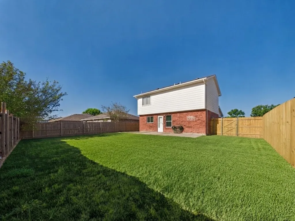 Expansive backyard with a manicured lawn, full wood fencing, and a white exterior with a brick lower level