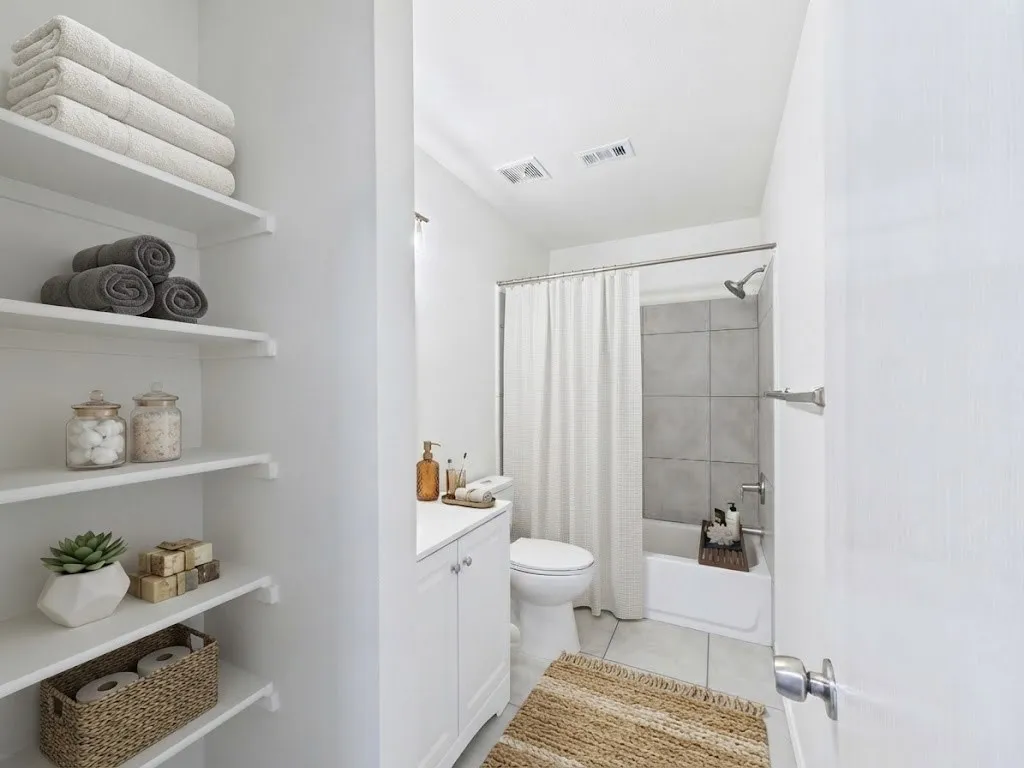 Recessed lighting illuminates the white bathtub and shower with gray tile surround, complemented by a white vanity with silver hardware