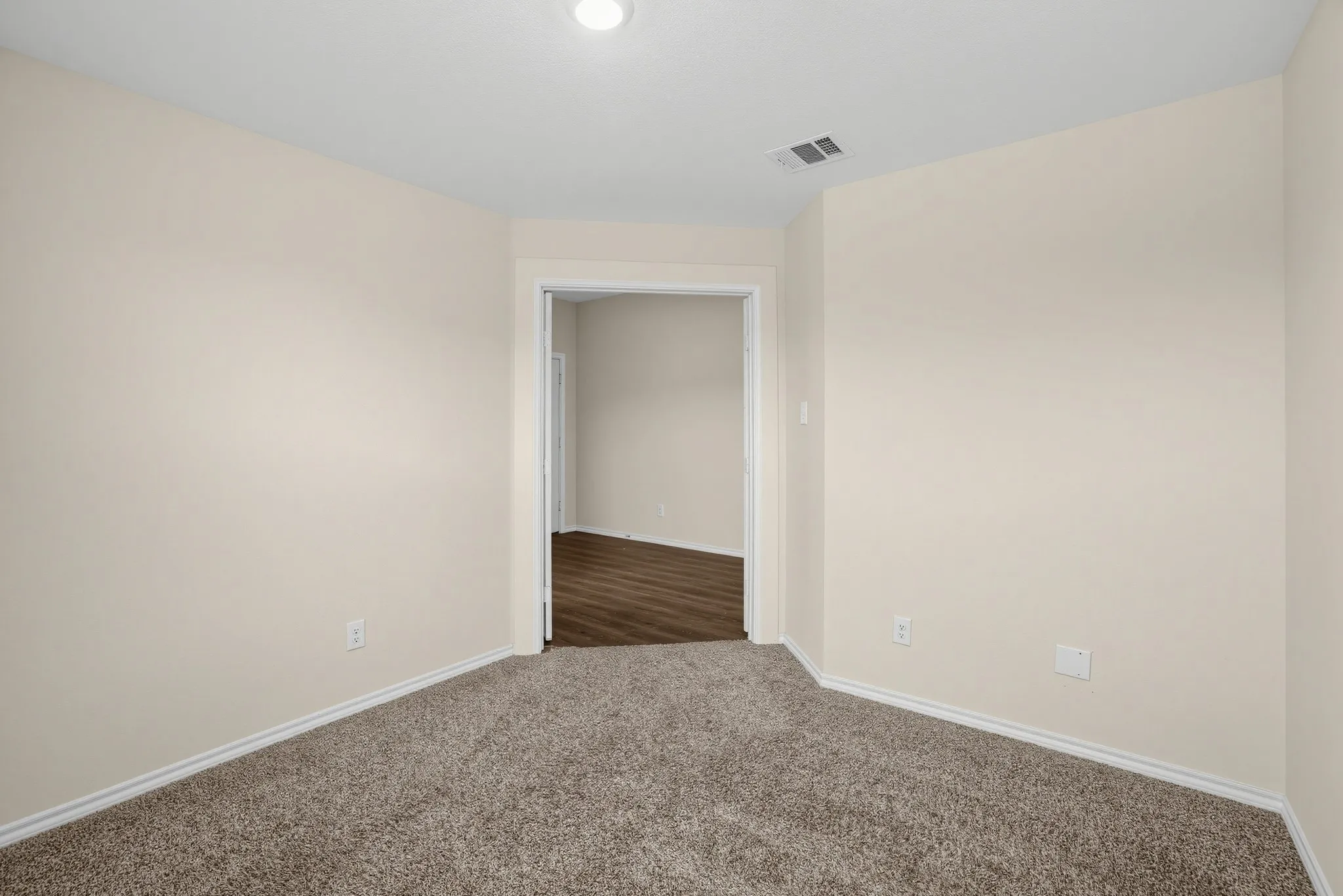 Neutral wall finishes, recessed ceiling lighting, textured carpet flooring, and an open doorway to an adjacent space with wood-finish flooring