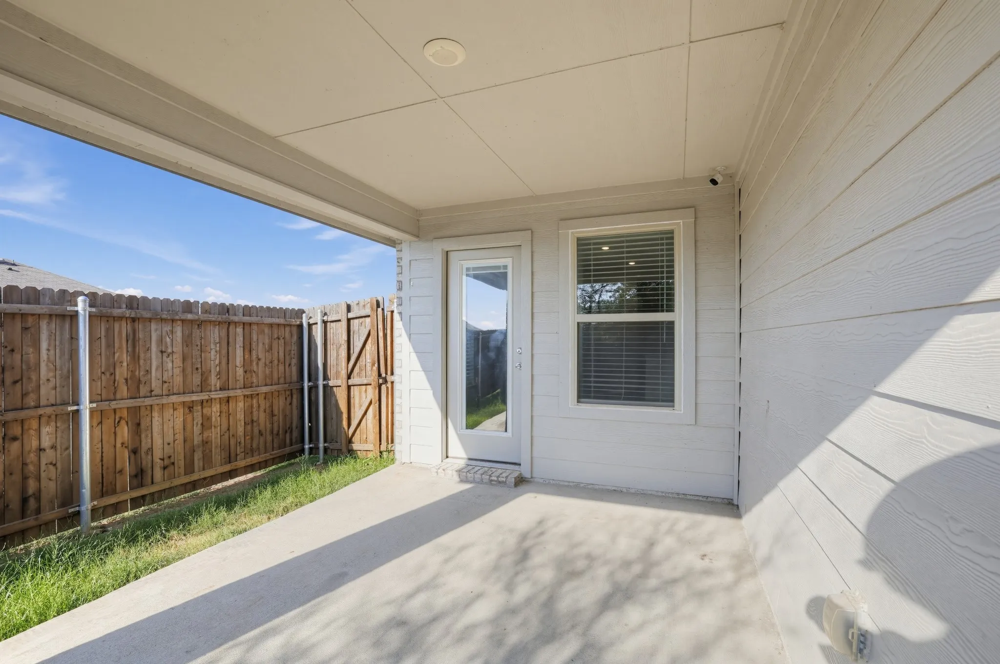 Covered patio with a concrete surface, featuring a wood fence, a full-lite exterior door, and a window with blinds