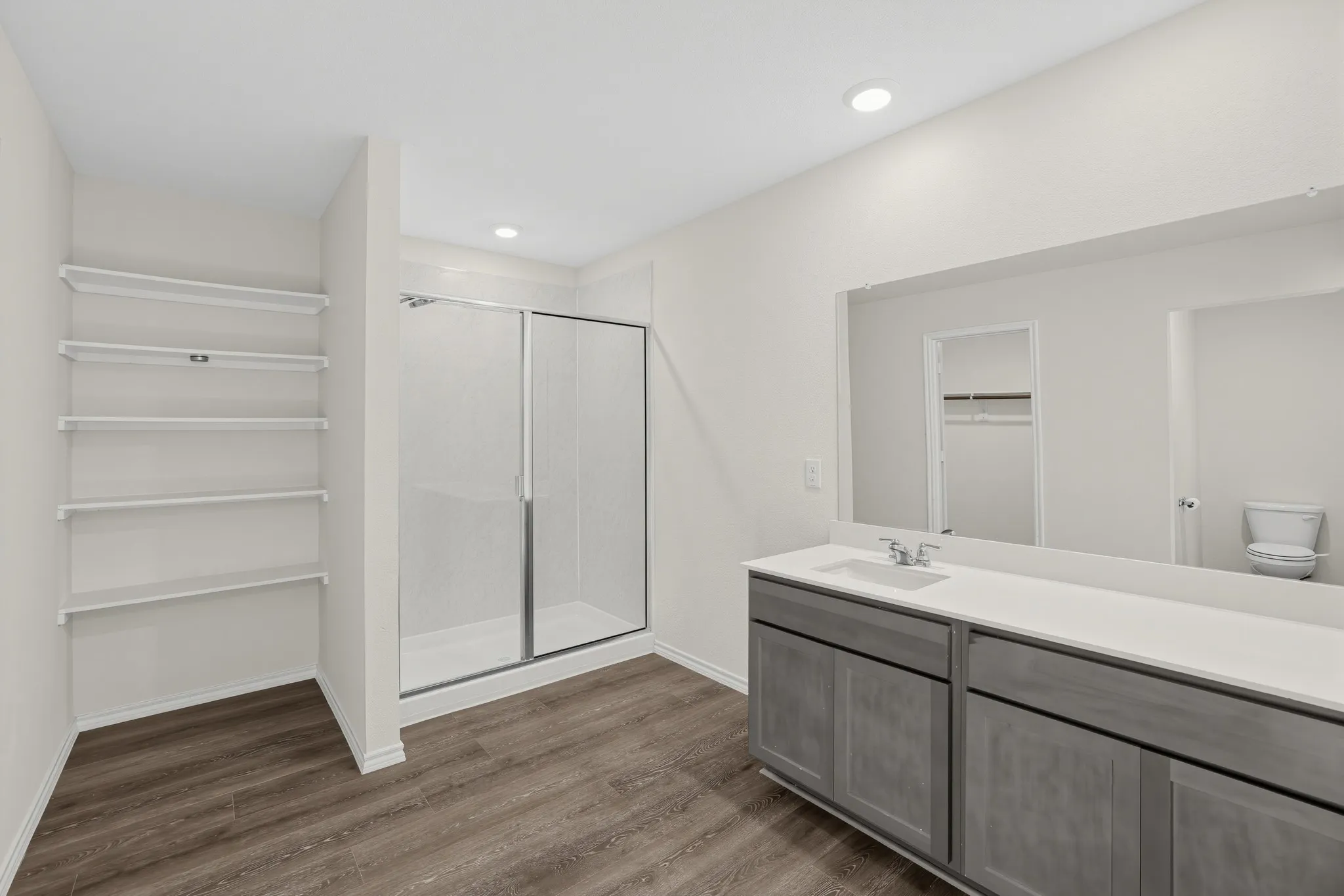 Wood-finish flooring, built-in shelving, glass-enclosed shower, dual vanity with undermount sink, and large wall mirror