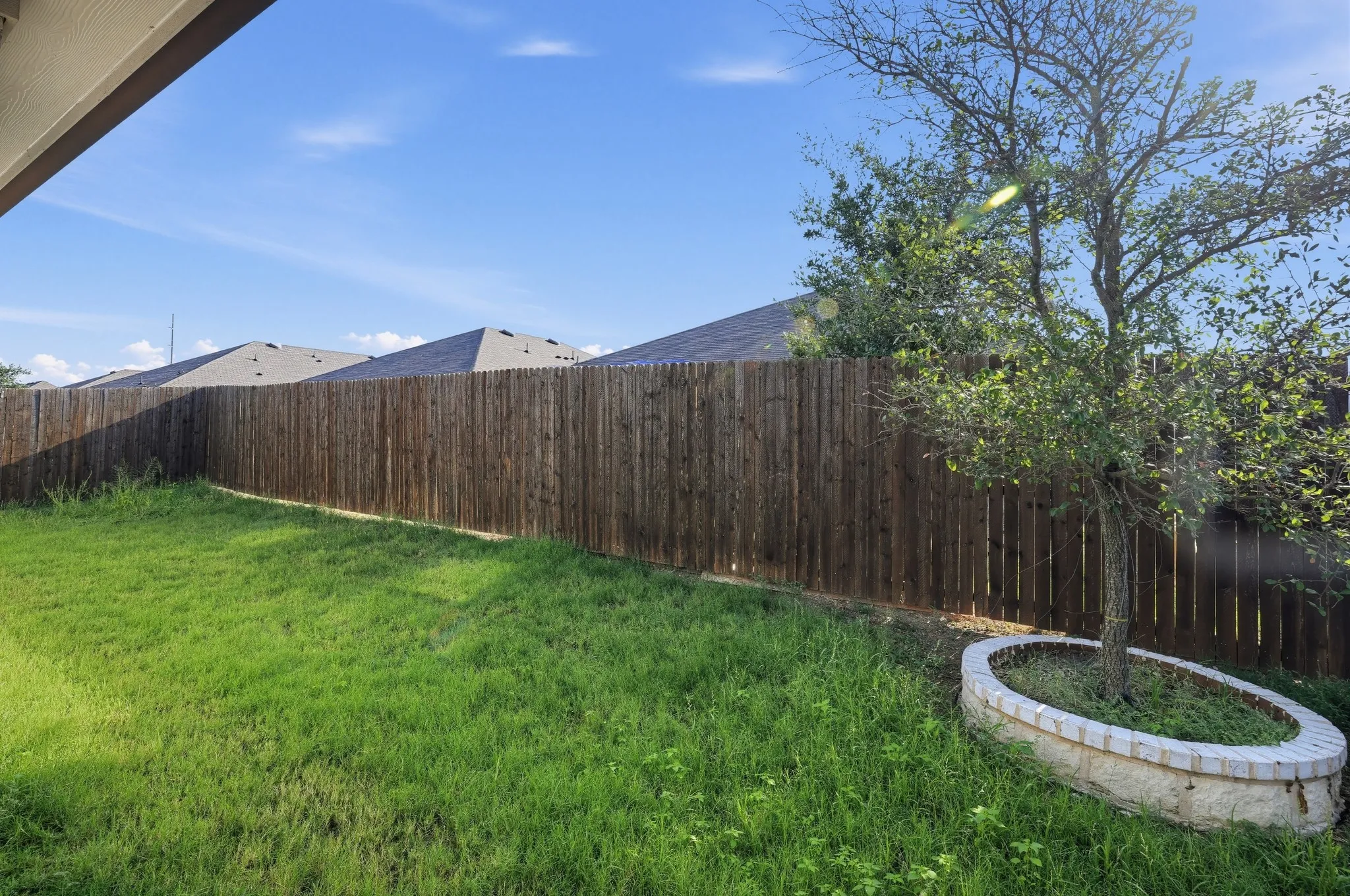 Expansive backyard featuring a wood privacy fence, a mature tree, and a stone-edged tree ring