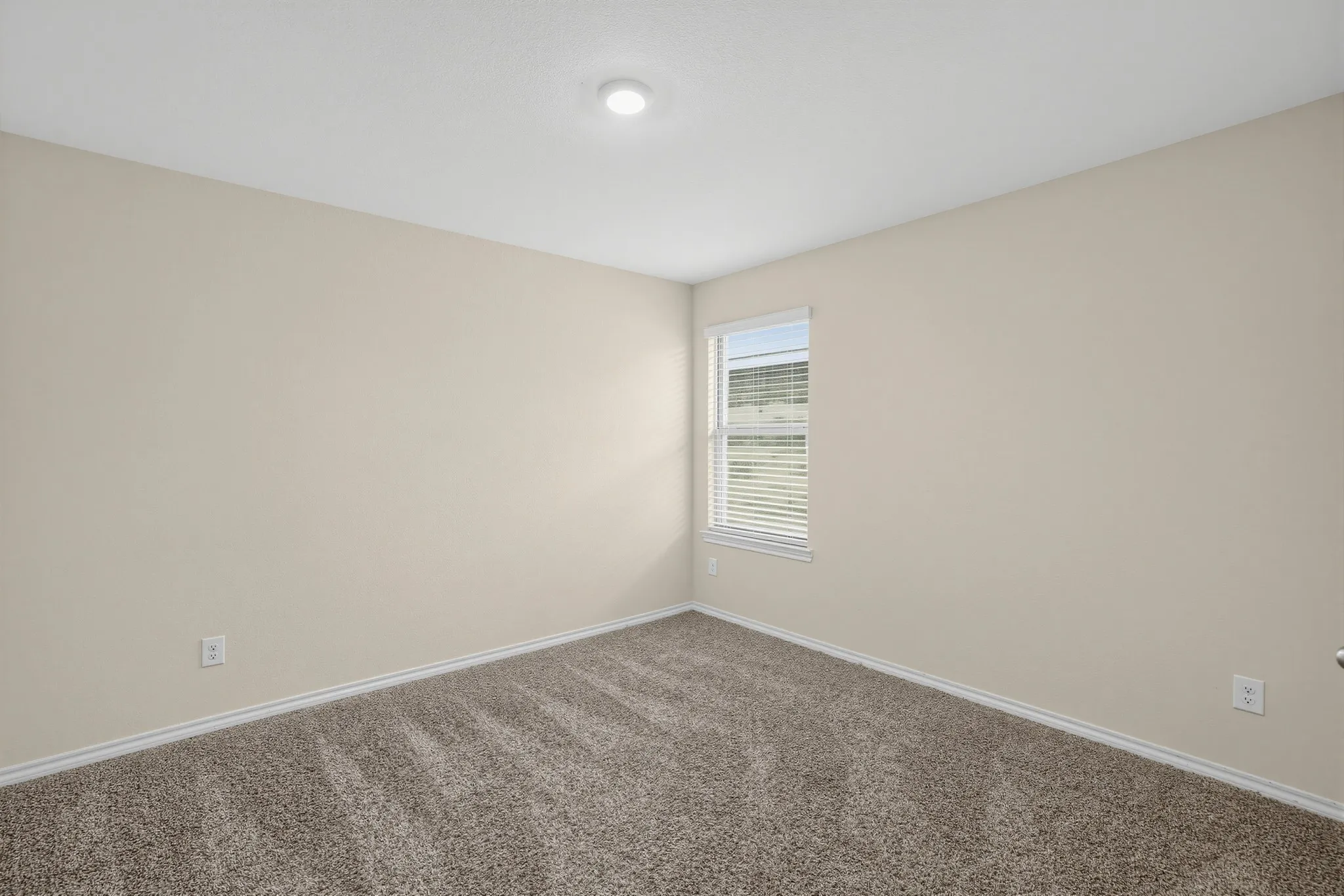 Recessed ceiling lighting, neutral wall tones, carpeted flooring, and a single window with blinds
