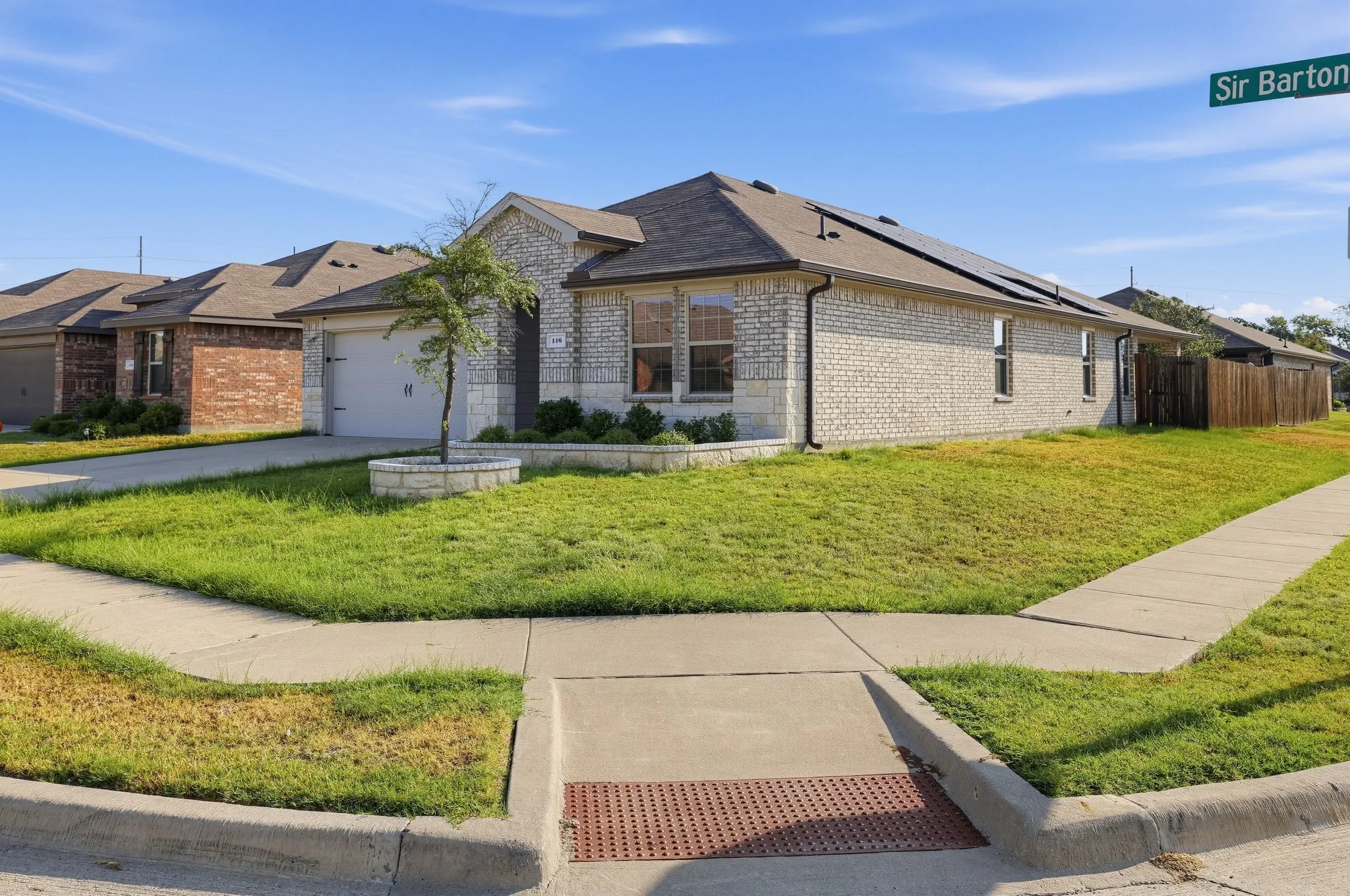 Brick and stone veneer exterior with an attached garage, paved driveway, and solar panels