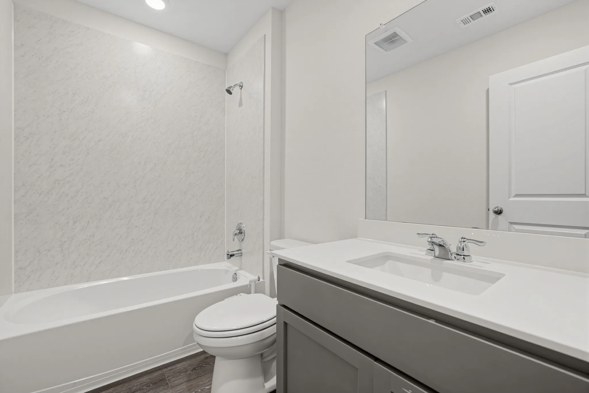 Tub/shower combination with a textured surround, single vanity with a white countertop and integrated sink, chrome fixtures, and wood-finish flooring