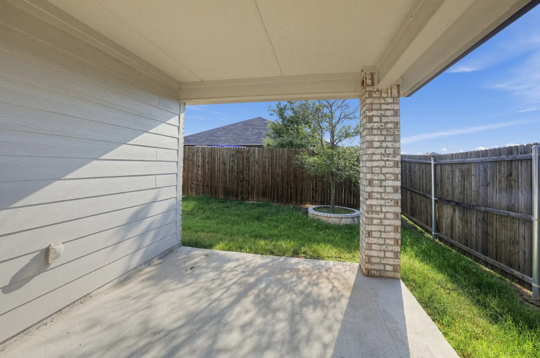 Covered outdoor patio with a concrete surface, a brick support column, and a wood privacy fence