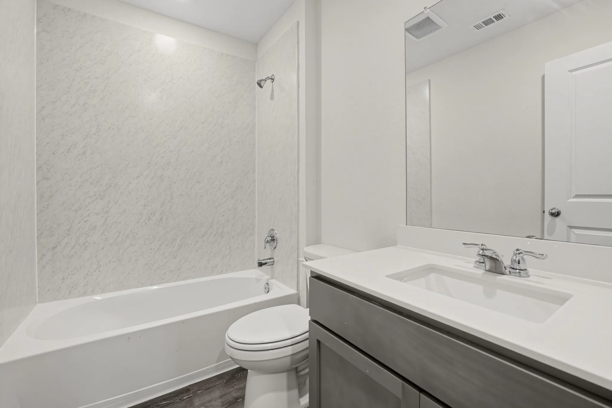 White bath-shower combination with chrome fixtures, wood-finish flooring, a contemporary vanity with an integrated sink, and a large wall-mounted mirror