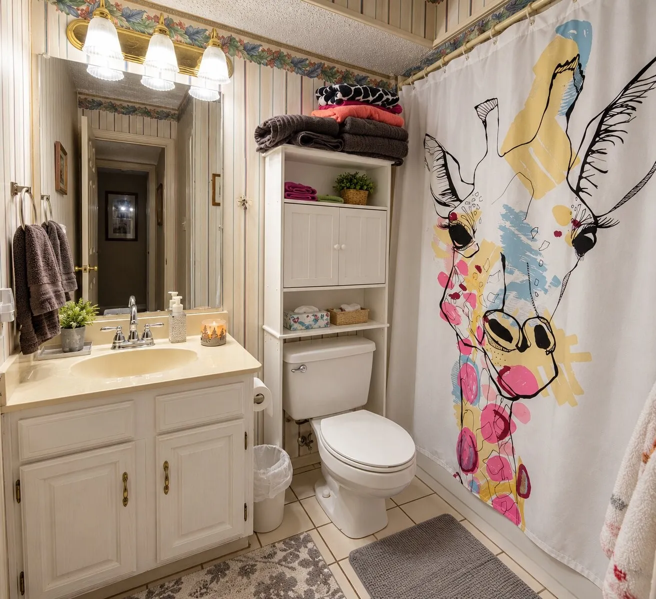 White vanity with a single basin sink and chrome faucet, large wall mirror, three-light fixture, built-in storage shelving, and a toilet