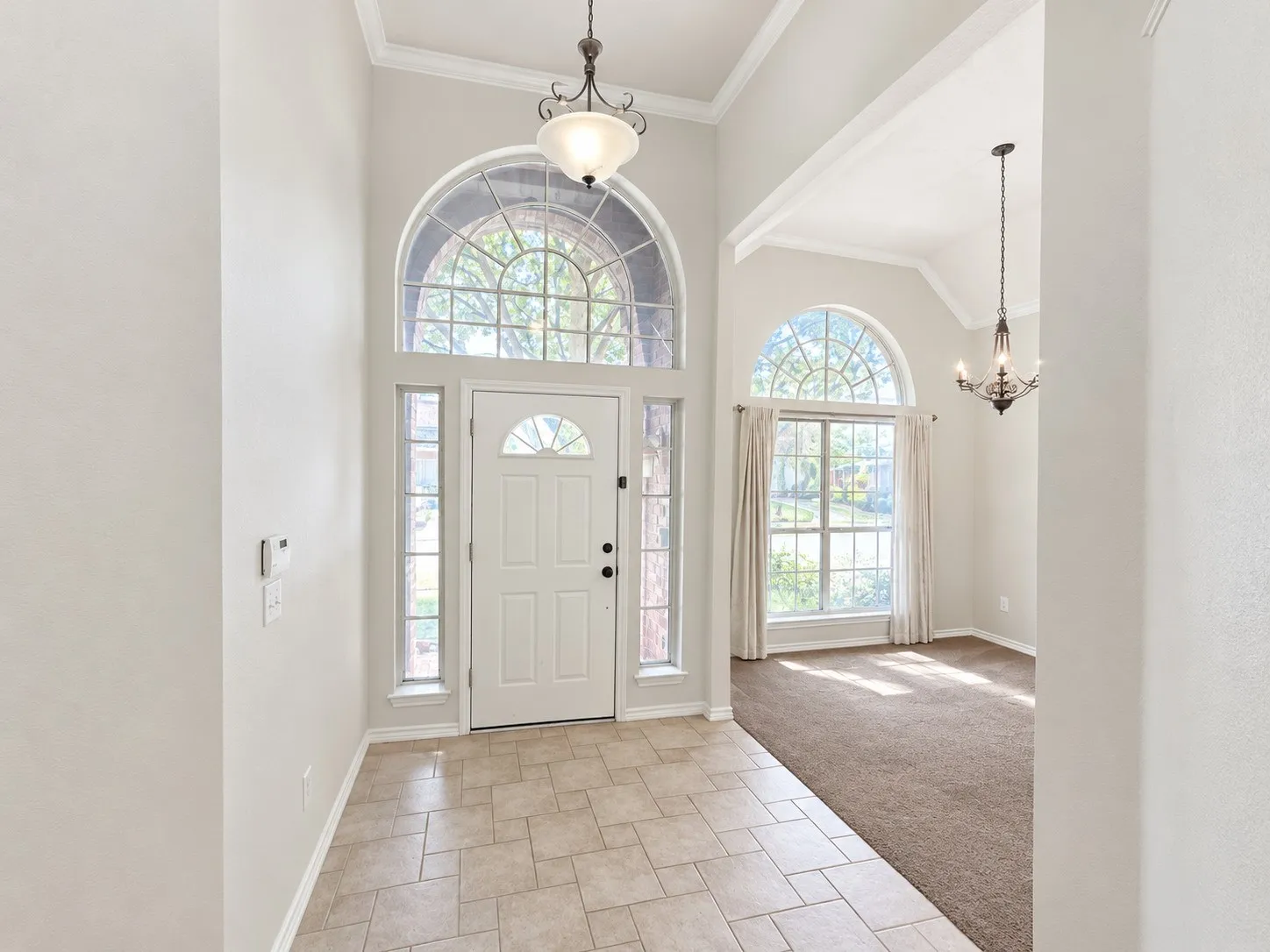 Entry foyer with vaulted ceiling, arched transom windows, tile flooring, and decorative chandeliers