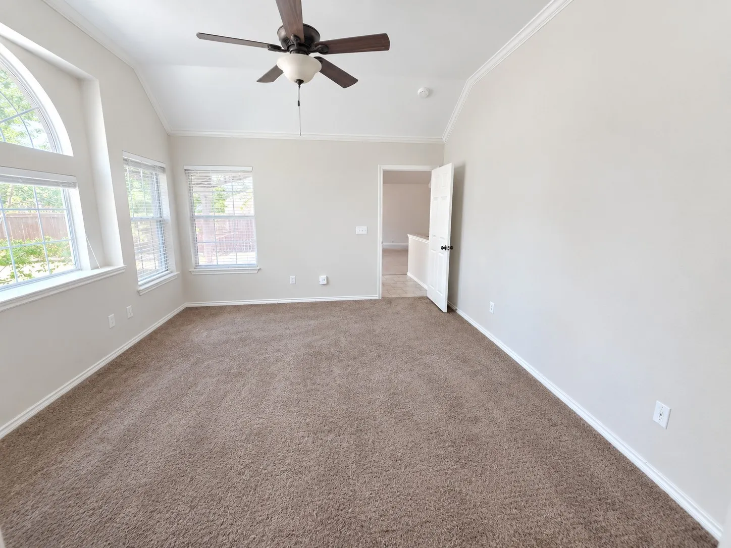 Vaulted ceiling with crown molding, ceiling fan, multiple windows with blinds, and neutral carpeting