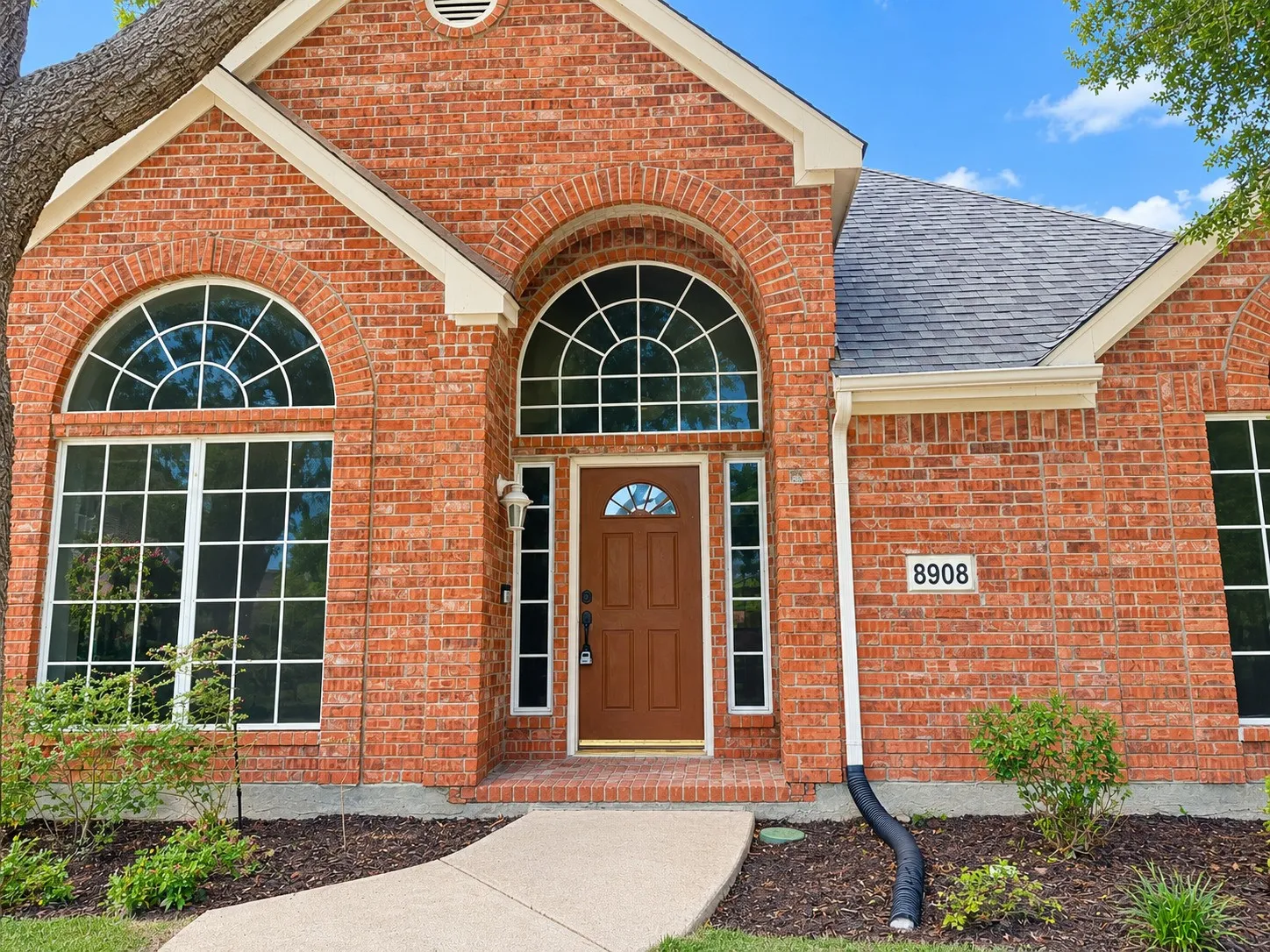 Red brick exterior with arched windows, a covered entry, and dark shingle roofing