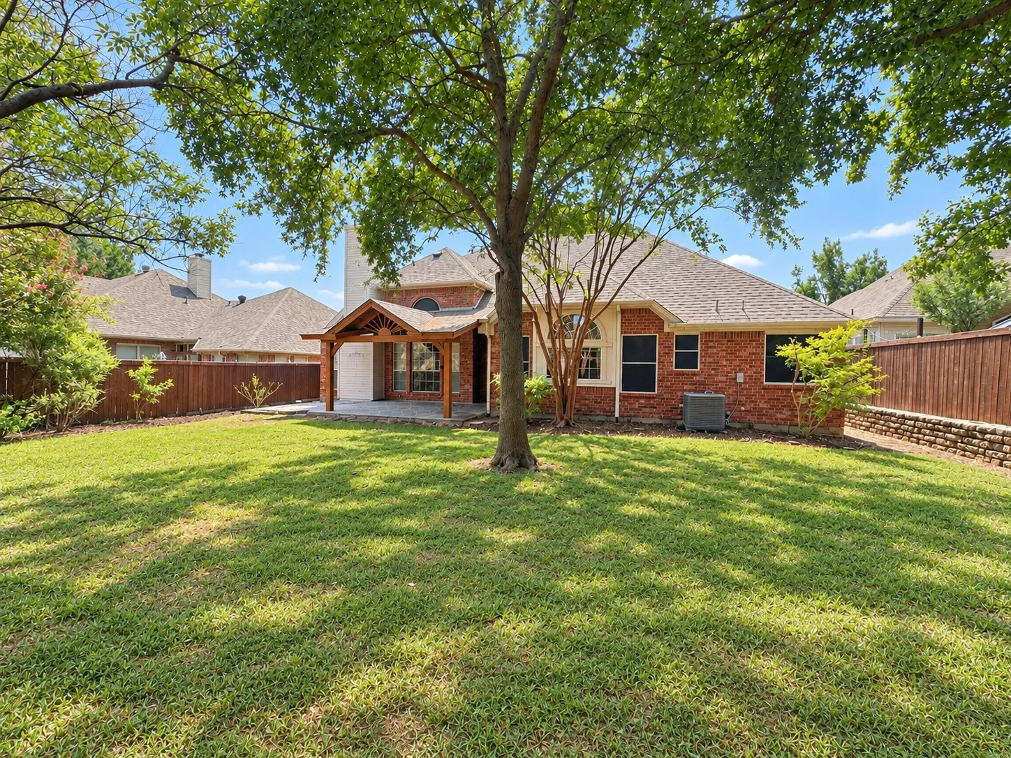Expansive backyard featuring a manicured lawn, mature trees, and a wooden privacy fence