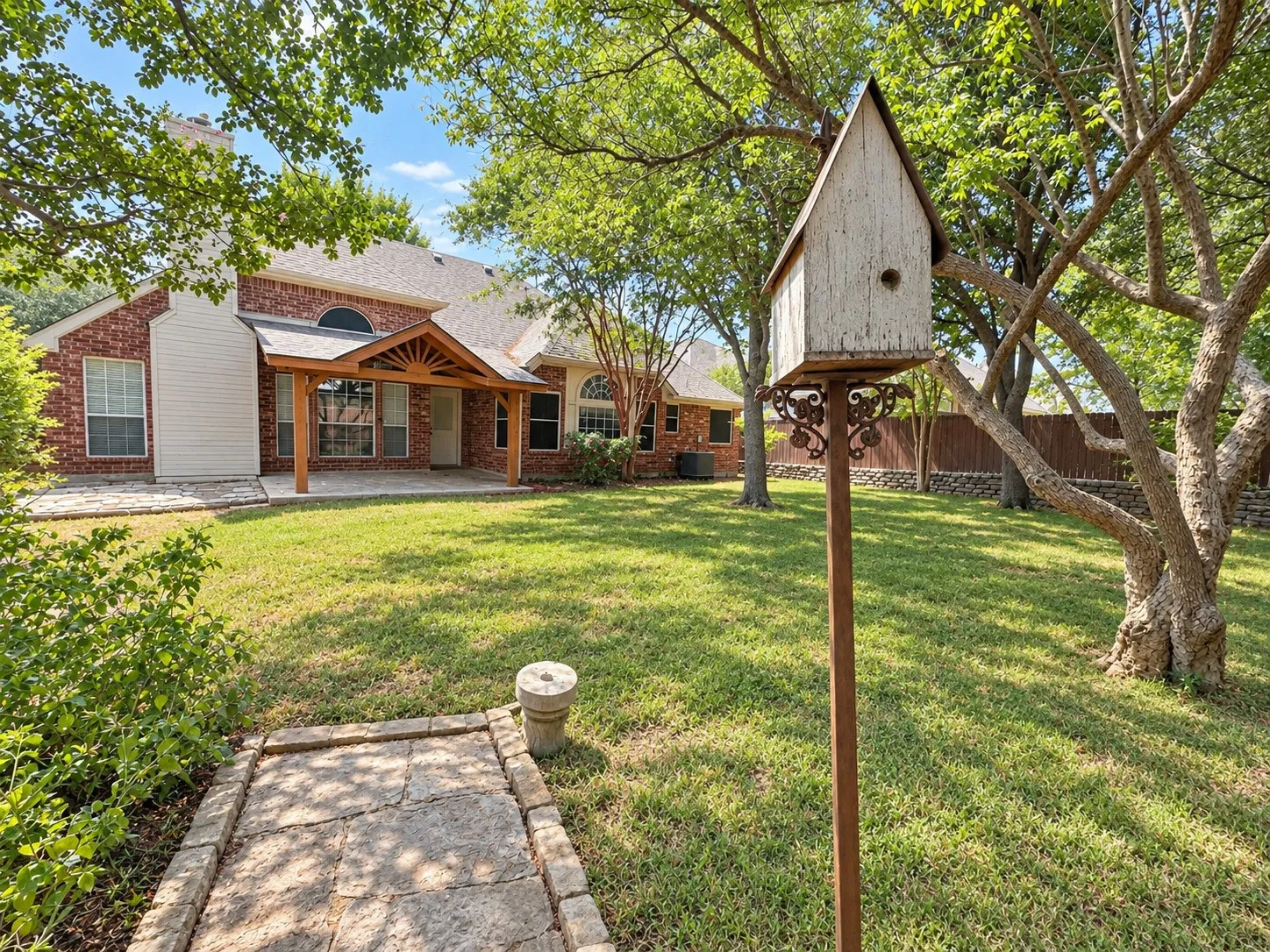 Expansive green lawn with mature trees and a stone-paved patio