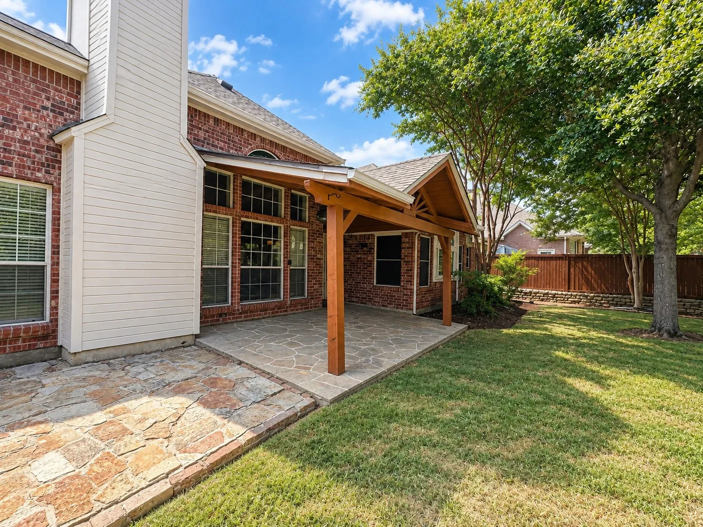 Expansive patio with stone-look flooring, a wood-beam pergola, and a brick exterior