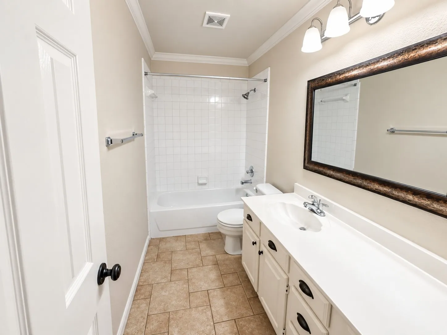 Bathroom featuring a white vanity with integrated sink, a rectangular framed mirror, a tub/shower combination with white subway tile surround, and neutral-toned tile flooring