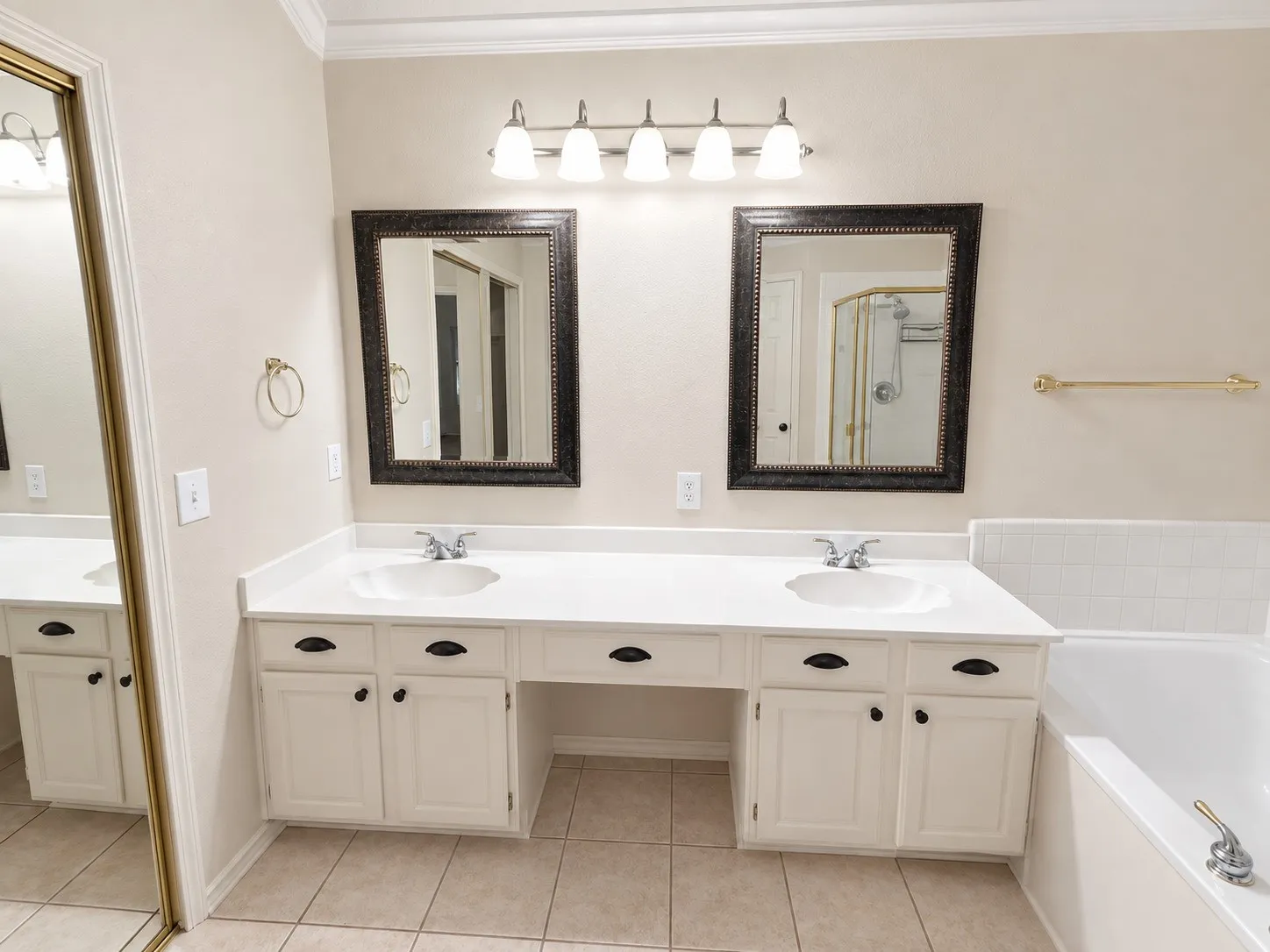 Dual vanity with integrated sinks, recessed bathtub, gold-framed glass shower enclosure, and tiled flooring