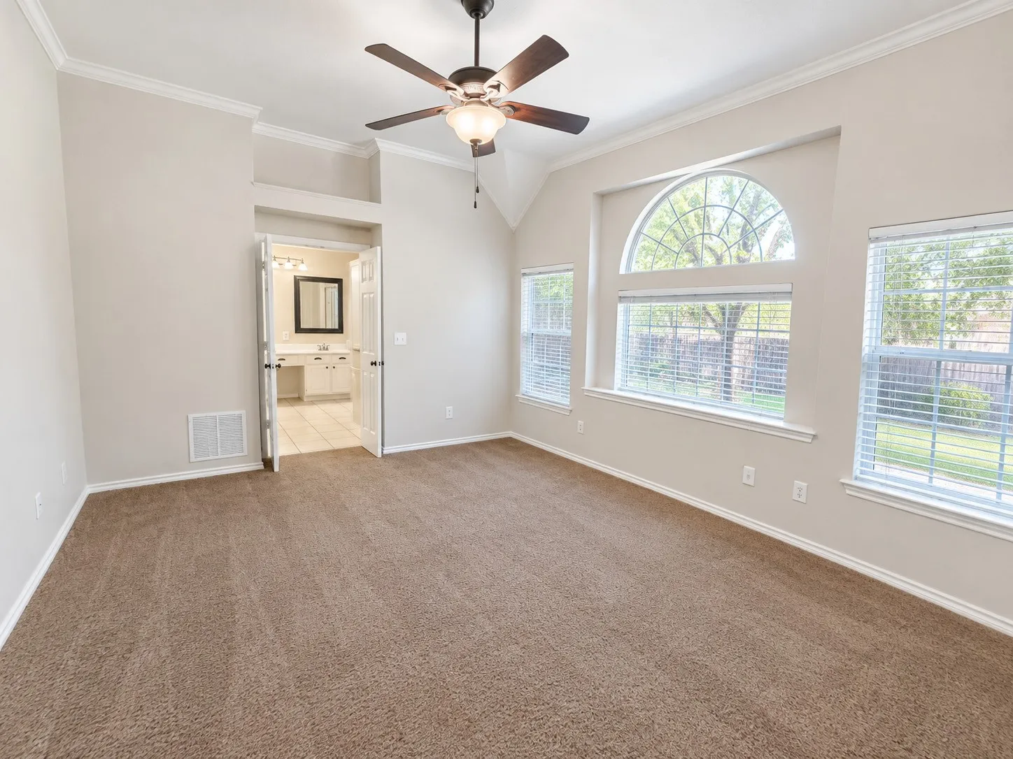 Vaulted ceiling with a ceiling fan, carpeted flooring, and multiple windows, including an arched window