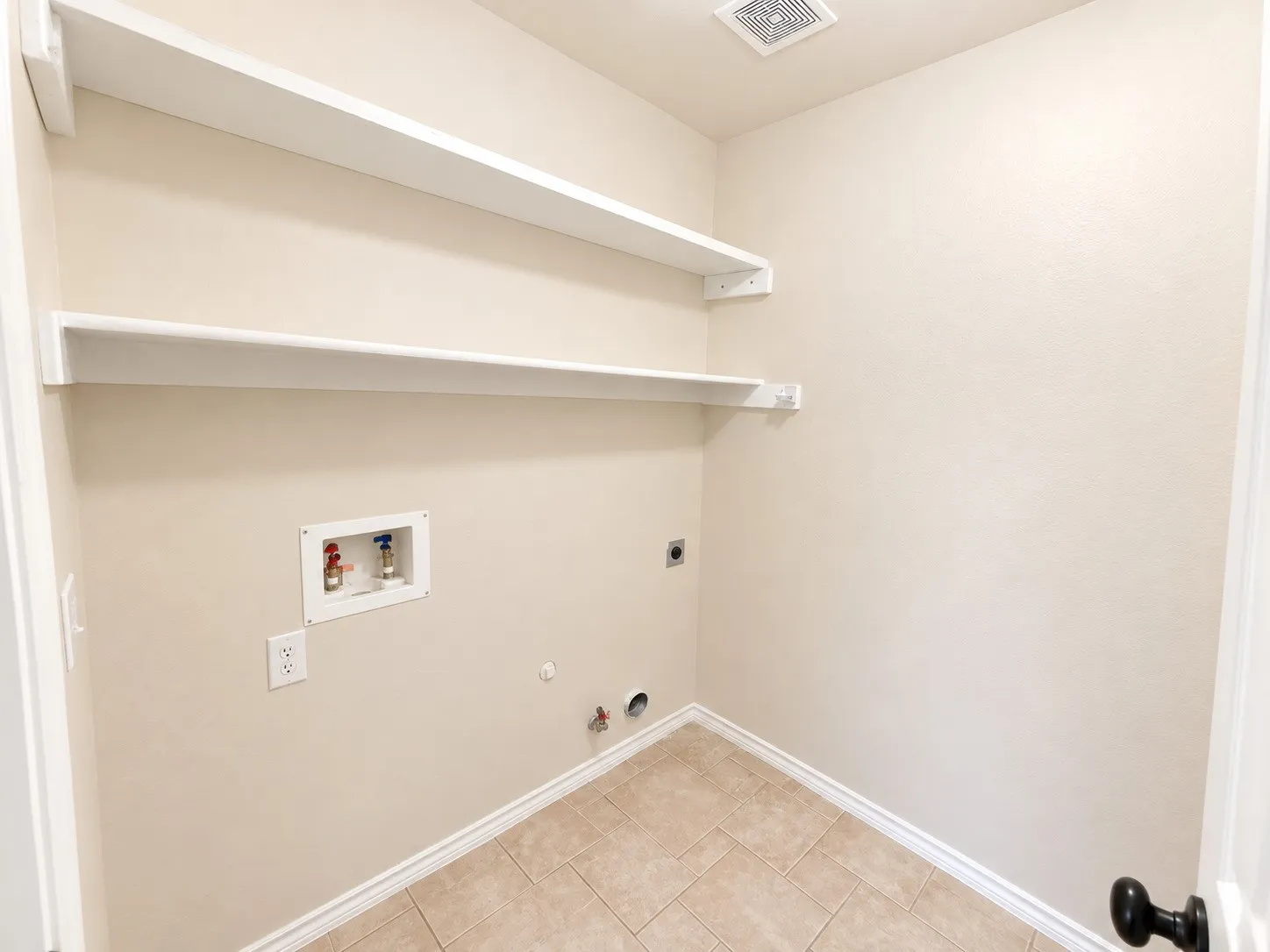 Laundry area with tile flooring, two wall-mounted shelves, and utility hookups