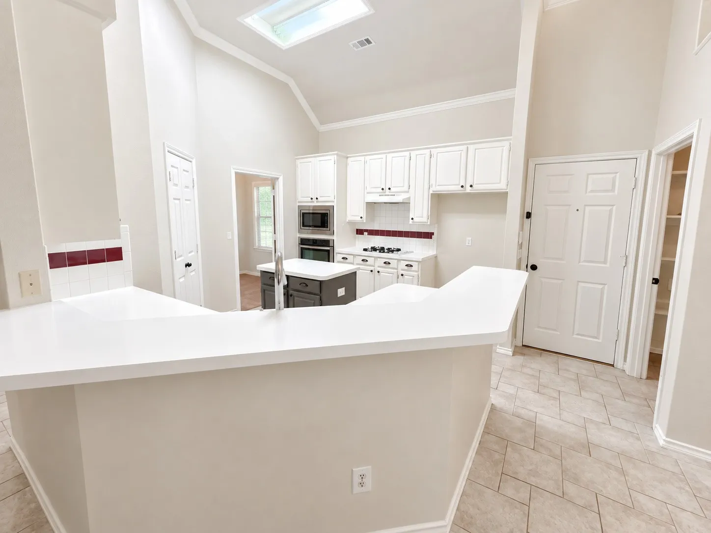 Vaulted ceiling with skylight, white cabinetry, dark island with sink, stainless steel appliances, and tile flooring