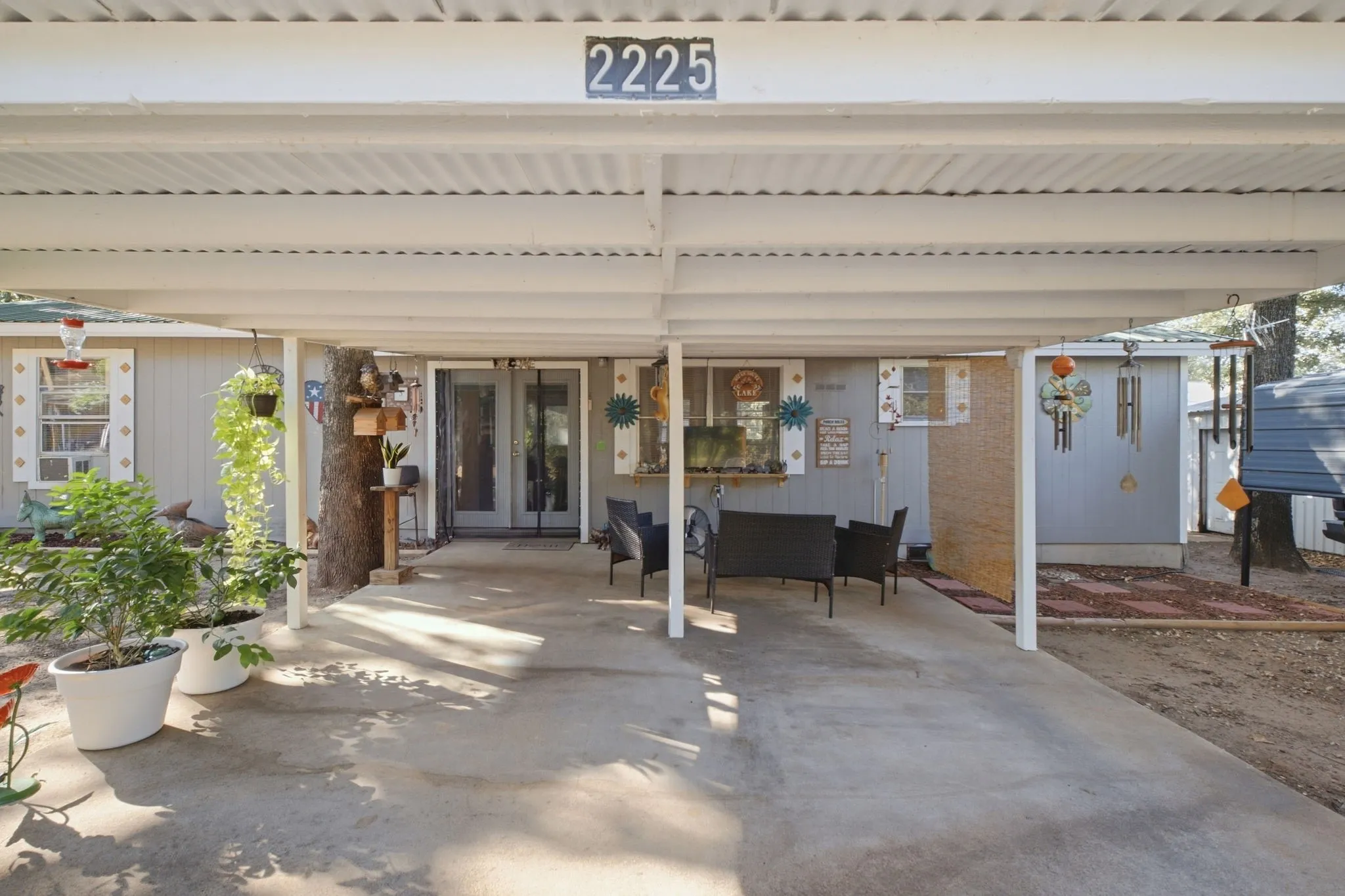 Covered carport with concrete flooring, showcasing a light gray exterior, white window trim, and a double-door entry