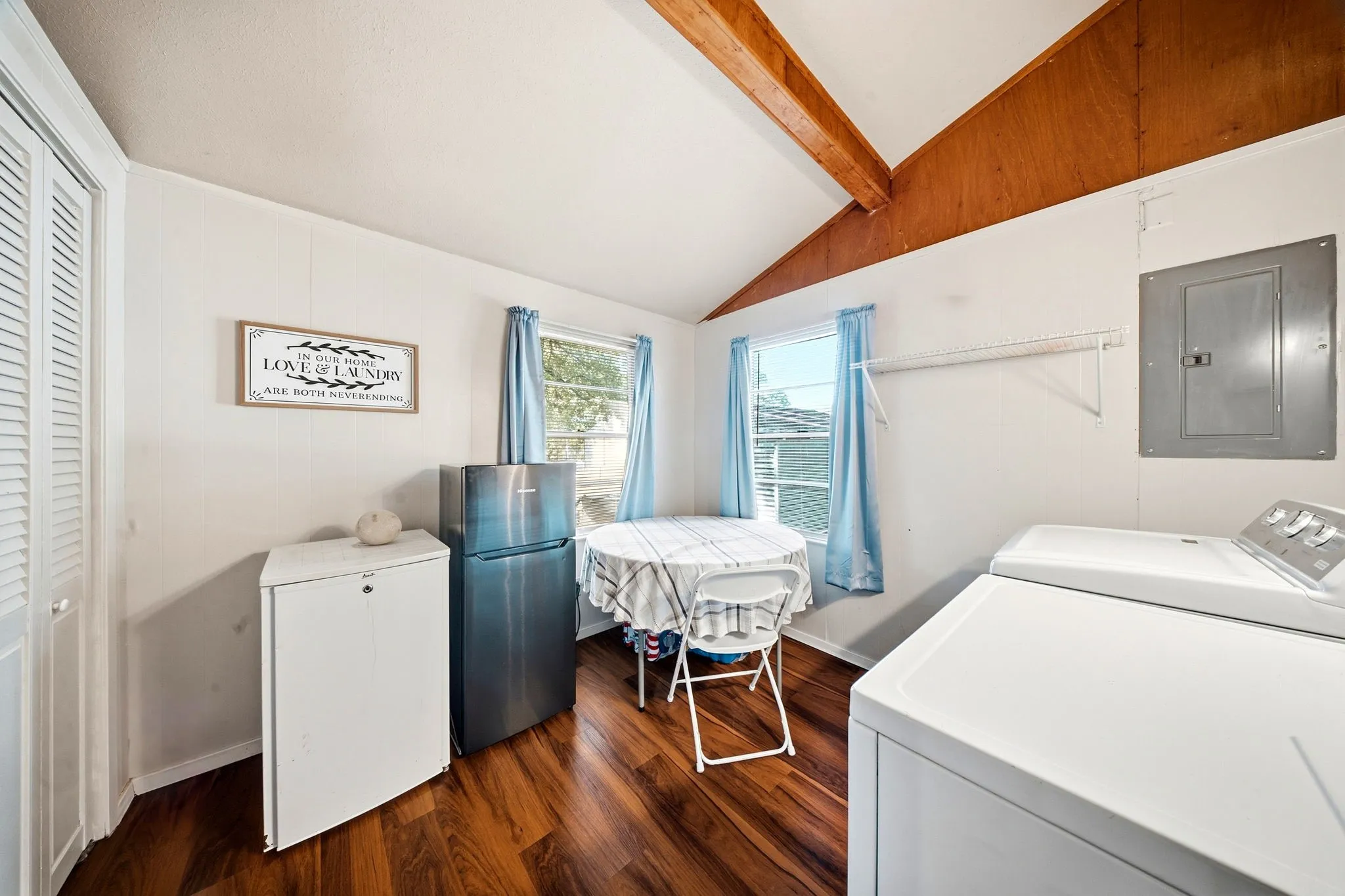 Vaulted ceiling with exposed wood beams, wood-finish flooring, and white paneled walls