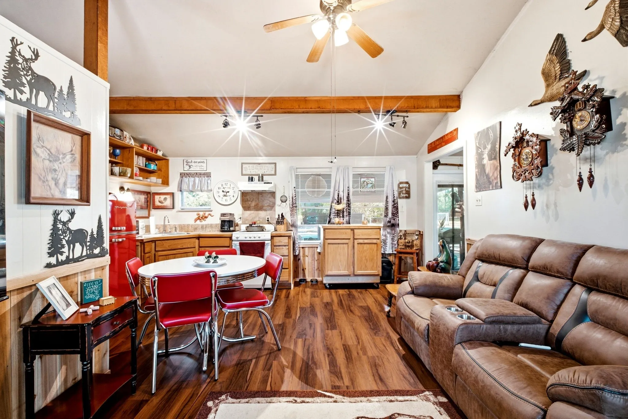Vaulted ceiling with wood beams, wood-finish flooring, kitchen with light wood cabinetry, ceiling fan, and track lighting