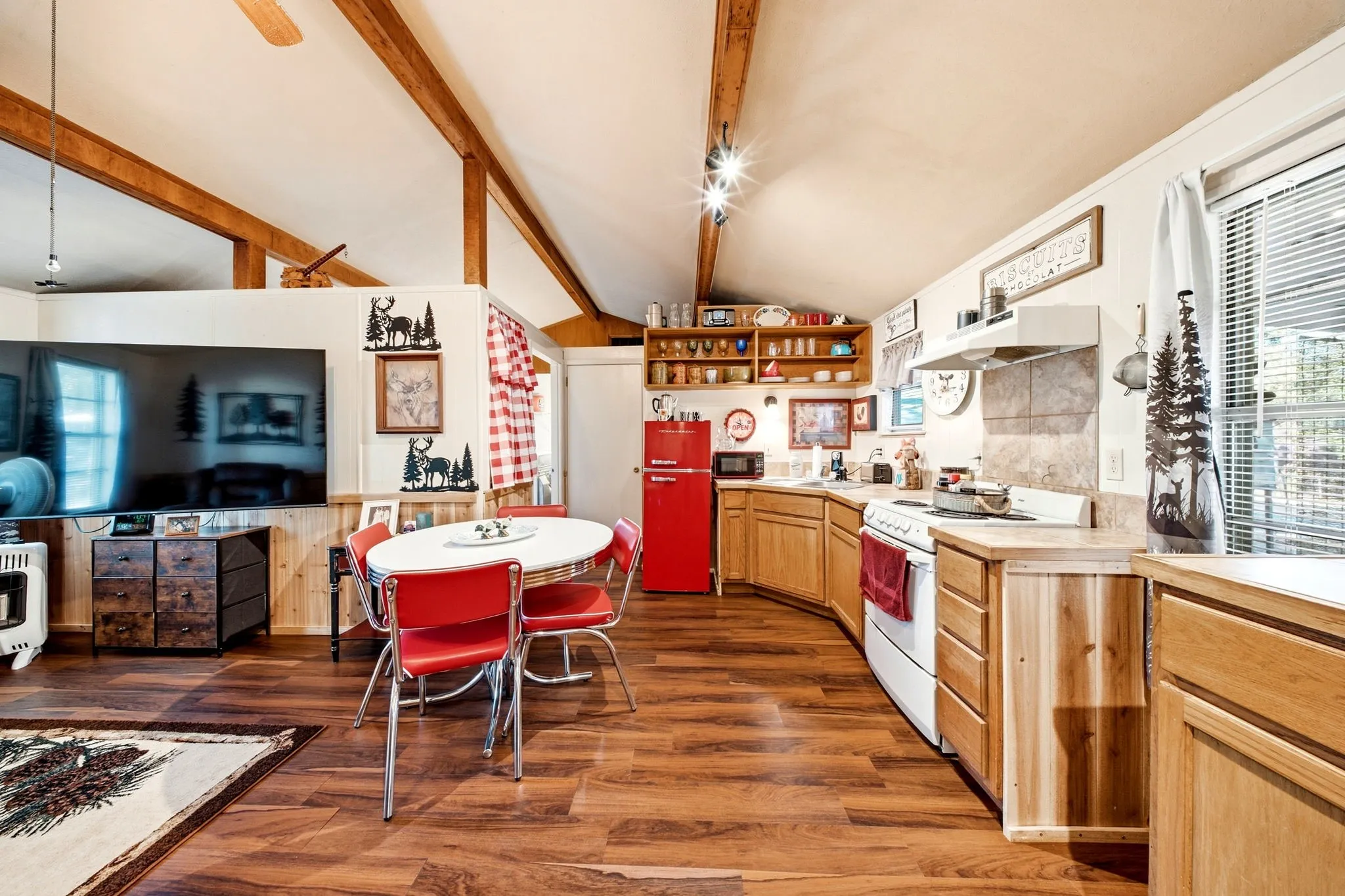 Vaulted ceiling with exposed wood beams, wood-finish flooring, wood-paneled accents, and kitchen with wood cabinetry