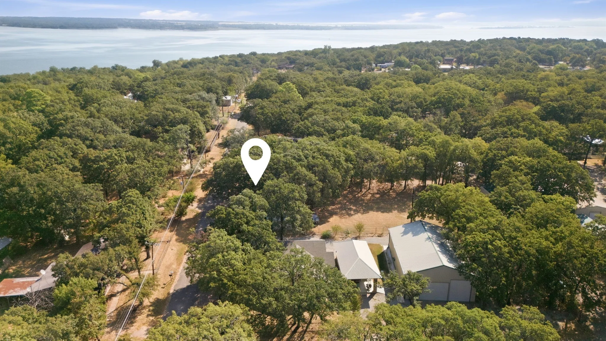 Wooded lot with a detached structure featuring a metal roof, located near a body of water